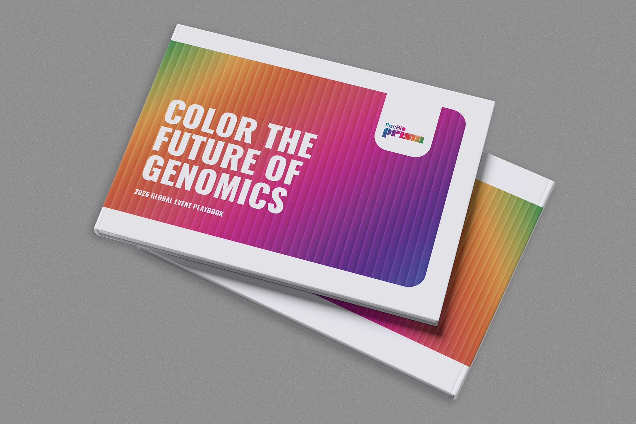 A stacked pair of PacBio PRISM 2026 Global Event Playbooks resting on a speckled grey surface, with the top booklet showing a bold, spectrum-striped cover and the white headline “COLOR THE FUTURE OF GENOMICS” above the subtitle “2026 GLOBAL EVENT PLAYBOOK,” alongside the PacBio prism logo in the upper right corner.