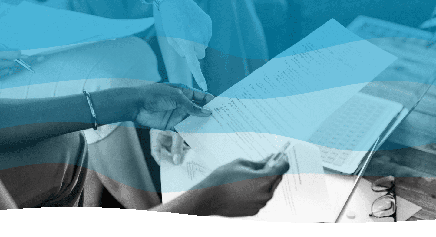 A person reviews documents held in their hands while sitting at a table, with a laptop nearby and a background featuring blue and white abstract waves.