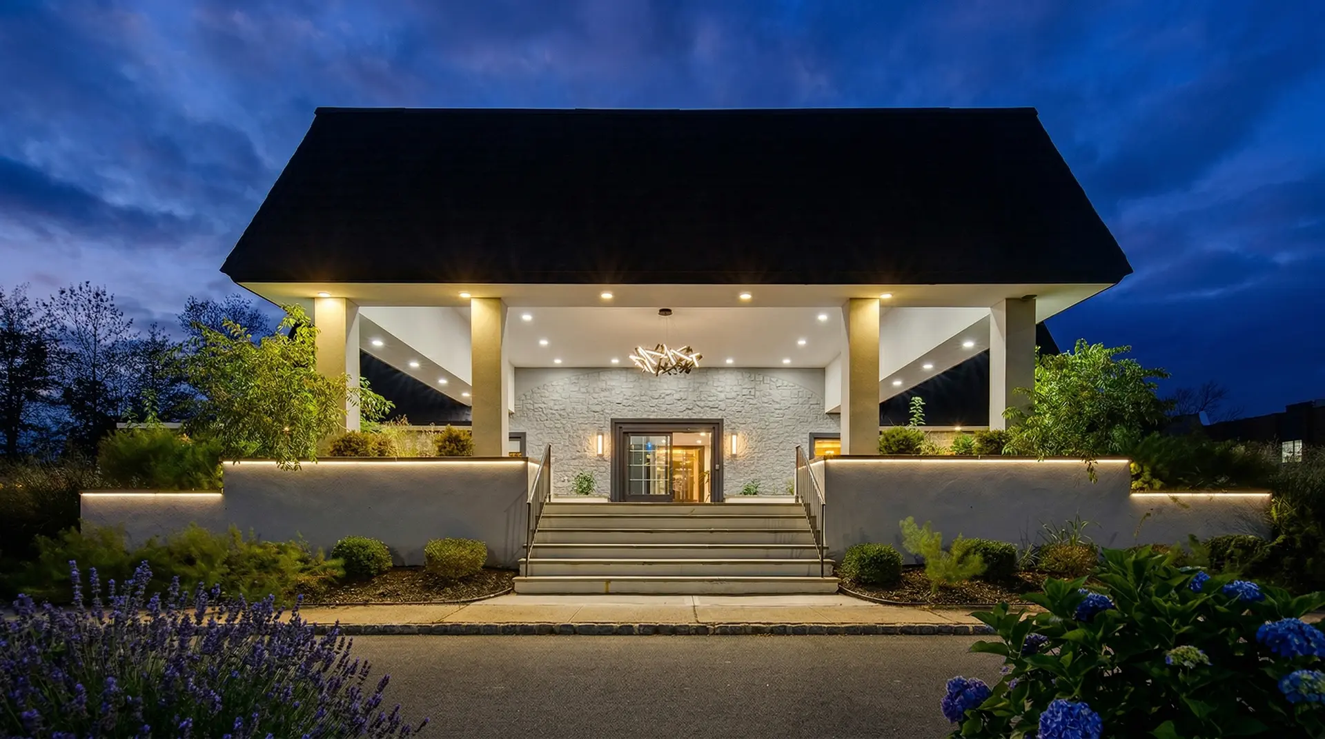 Illuminated building entrance with portico, stairs, and landscaping at night.