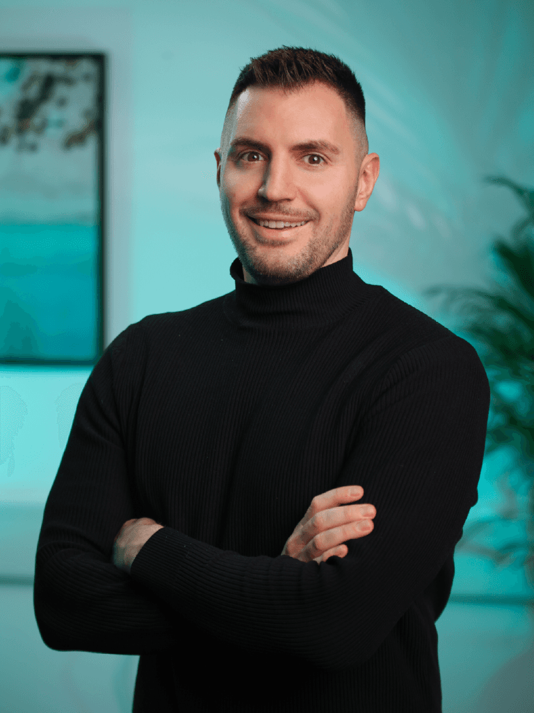 A woman with short curly hair wearing a black t-shirt looks into the camera.
