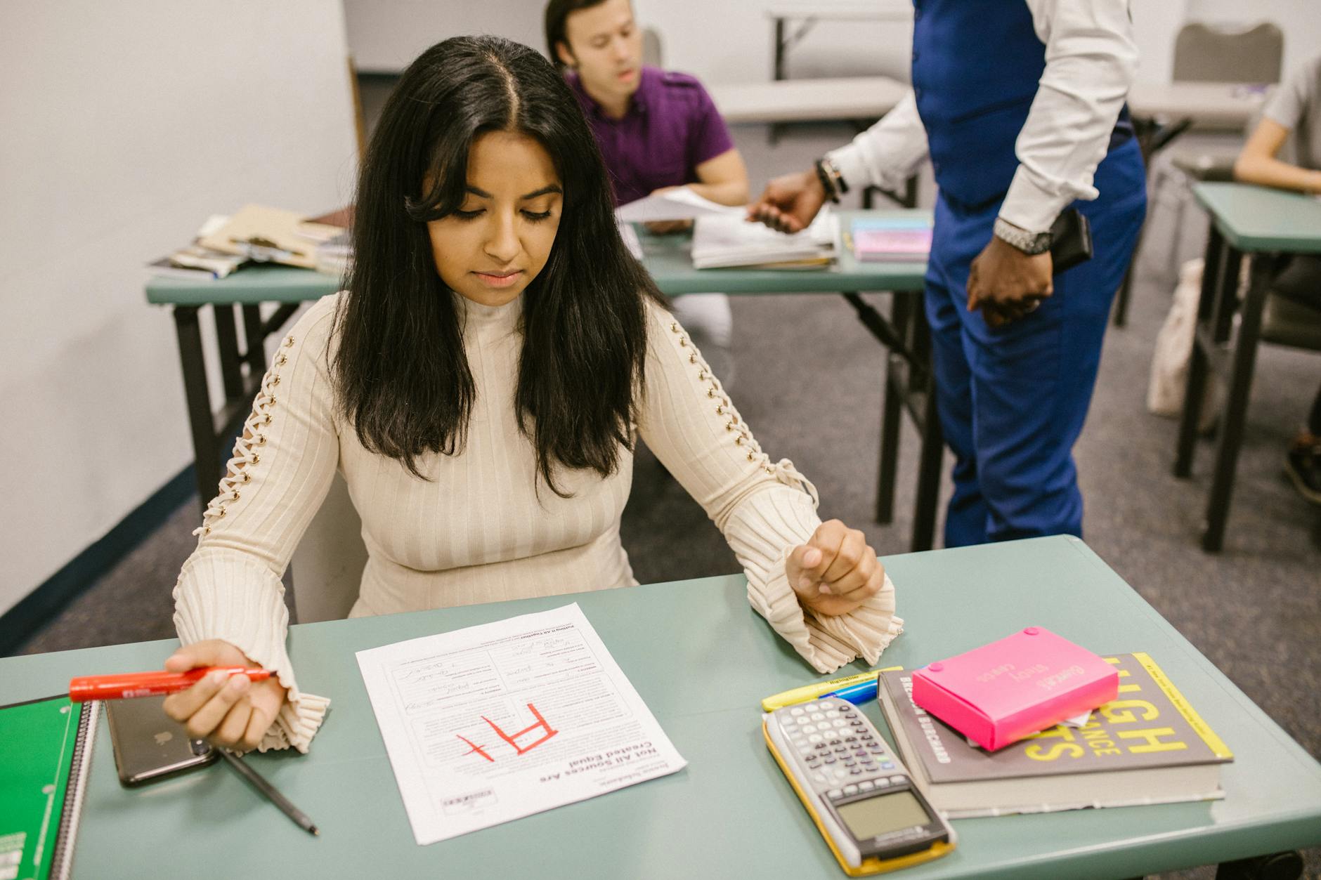 An instructor holding a digital tablet and checking off a rubric while observing students work in a chemistry lab.