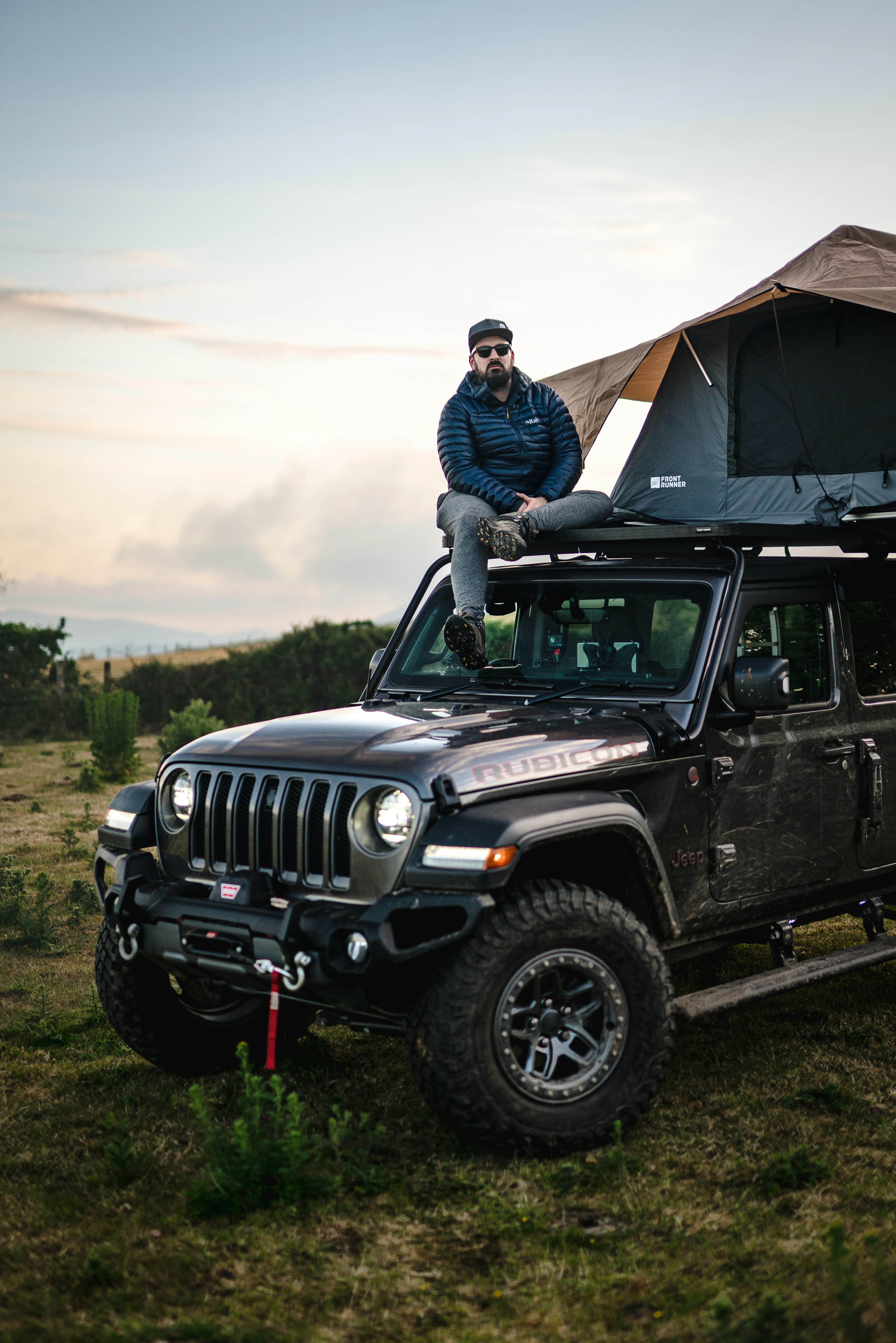 A man sits on top of his jeep with a rooftop tent, ready for the adventures that await.