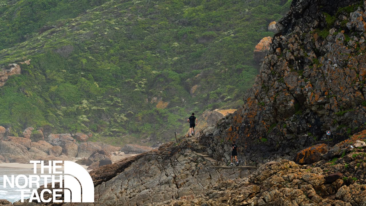 Trail runner running along the rocks of Robberg with the sea below them