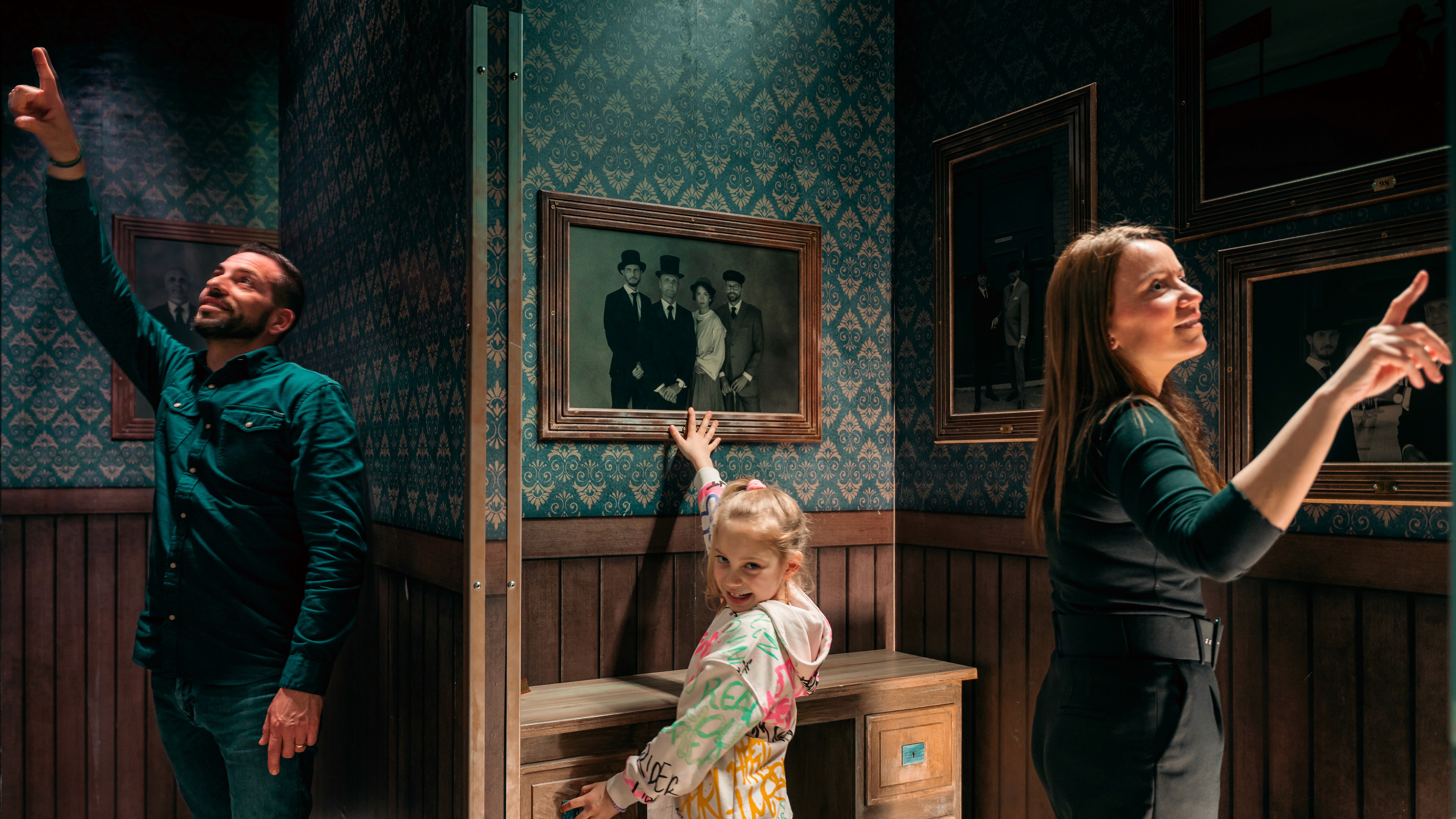 A young person with curly hair smiles at the camera while sitting in front of a laptop against a dark background.