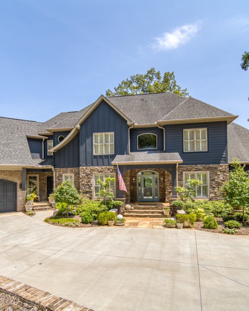 A smiling woman with her arms crossed, standing against a dark green background. She has long, dark hair.