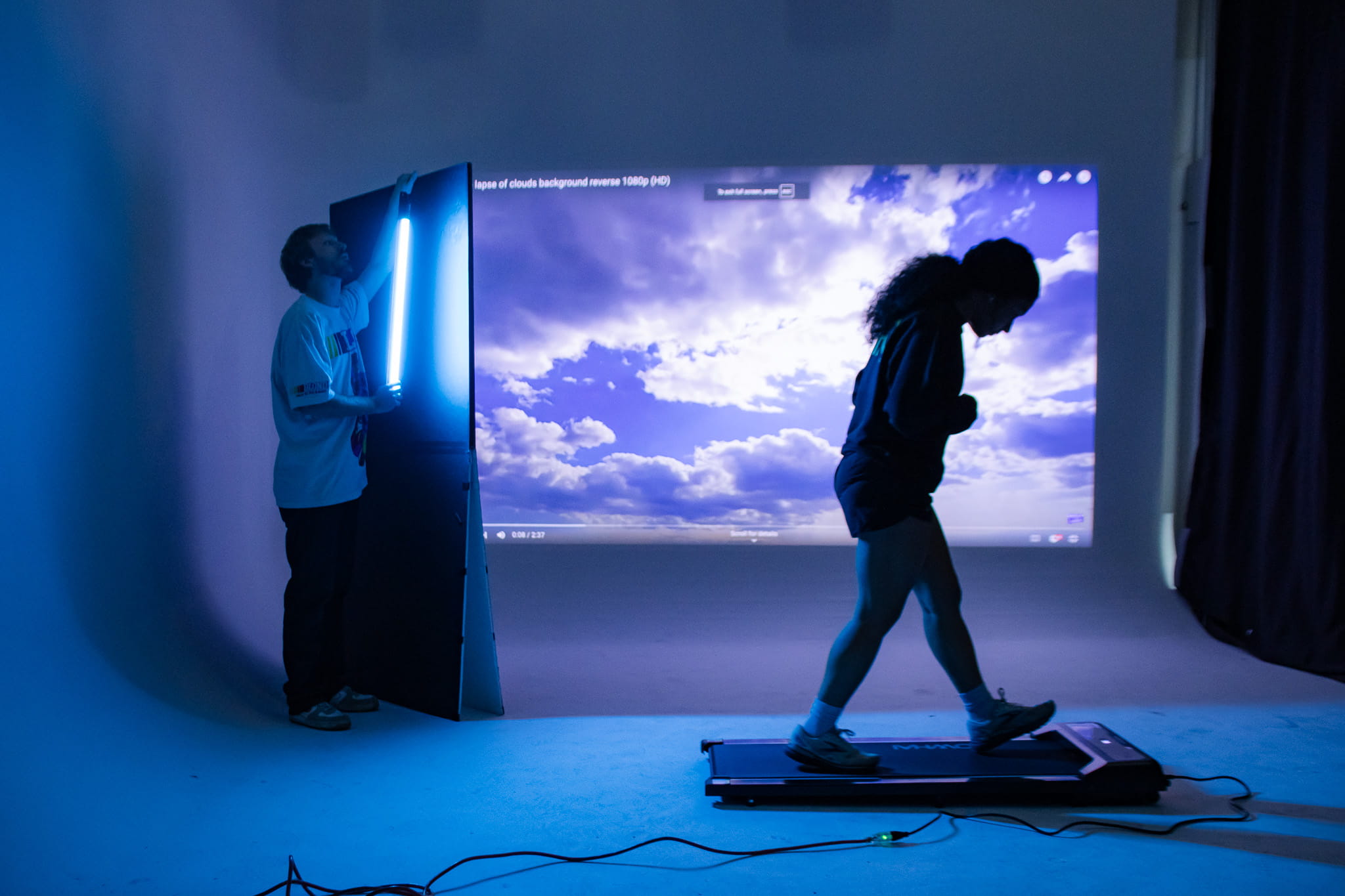 woman walks on a treadmill in front of a cloud scene projected onto a cyc wall for a race you home commercial shoot