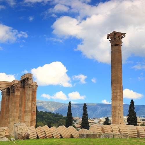 蓝天白云下,古希腊遗址矗立着高大的立柱,四周散落着石块,远处群山连绵。