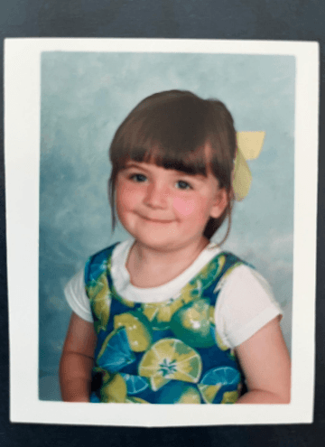 A couple stands on a sandy hill at sunset, facing away, with arms raised in a relaxed "hang loose" gesture. The scene conveys tranquility and joy.