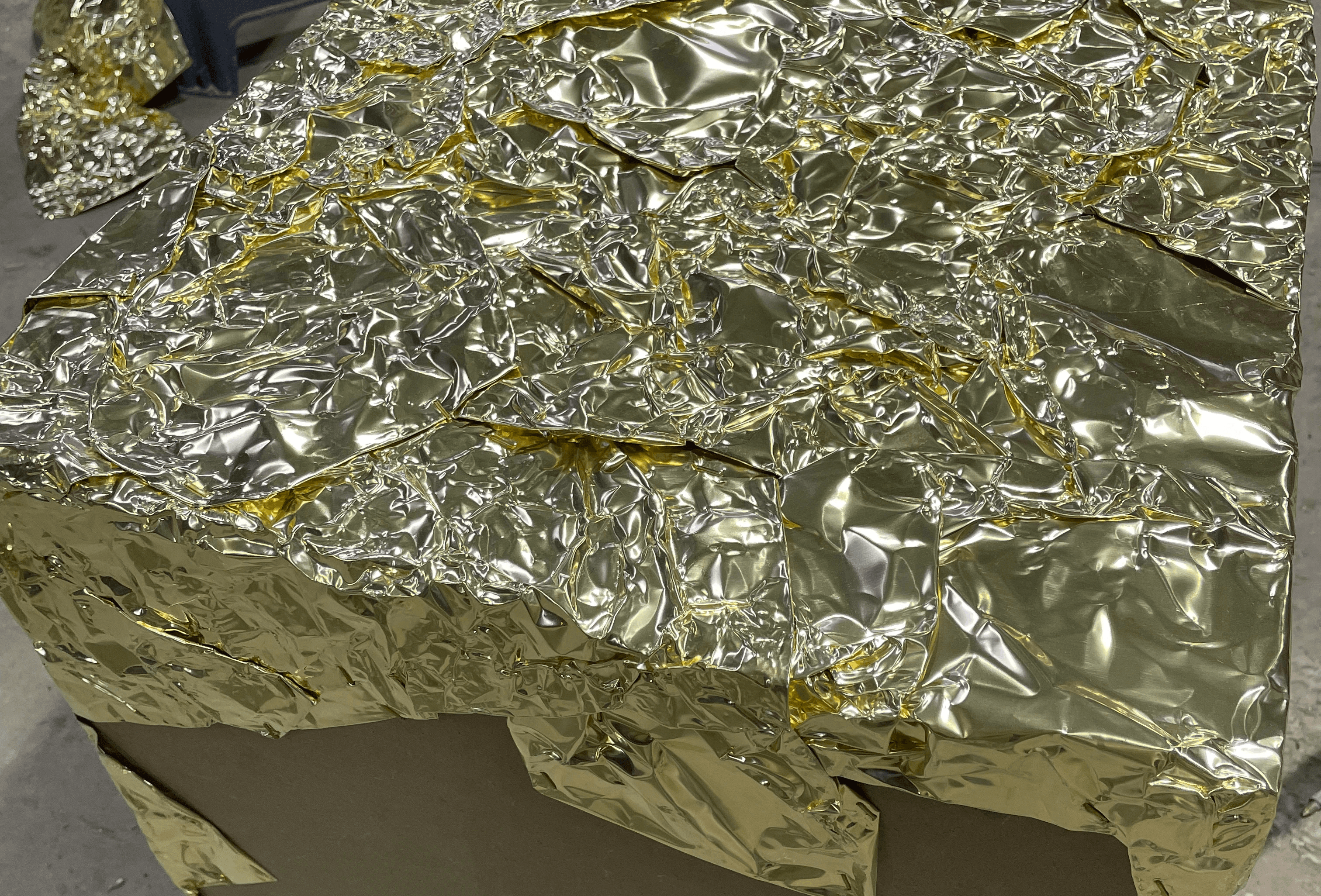 금박 시트를 구겨 접착한 큐브 표면 클로즈업, 불규칙한 반사 질감 / Close-up of crumpled gold foil texture on cube surface