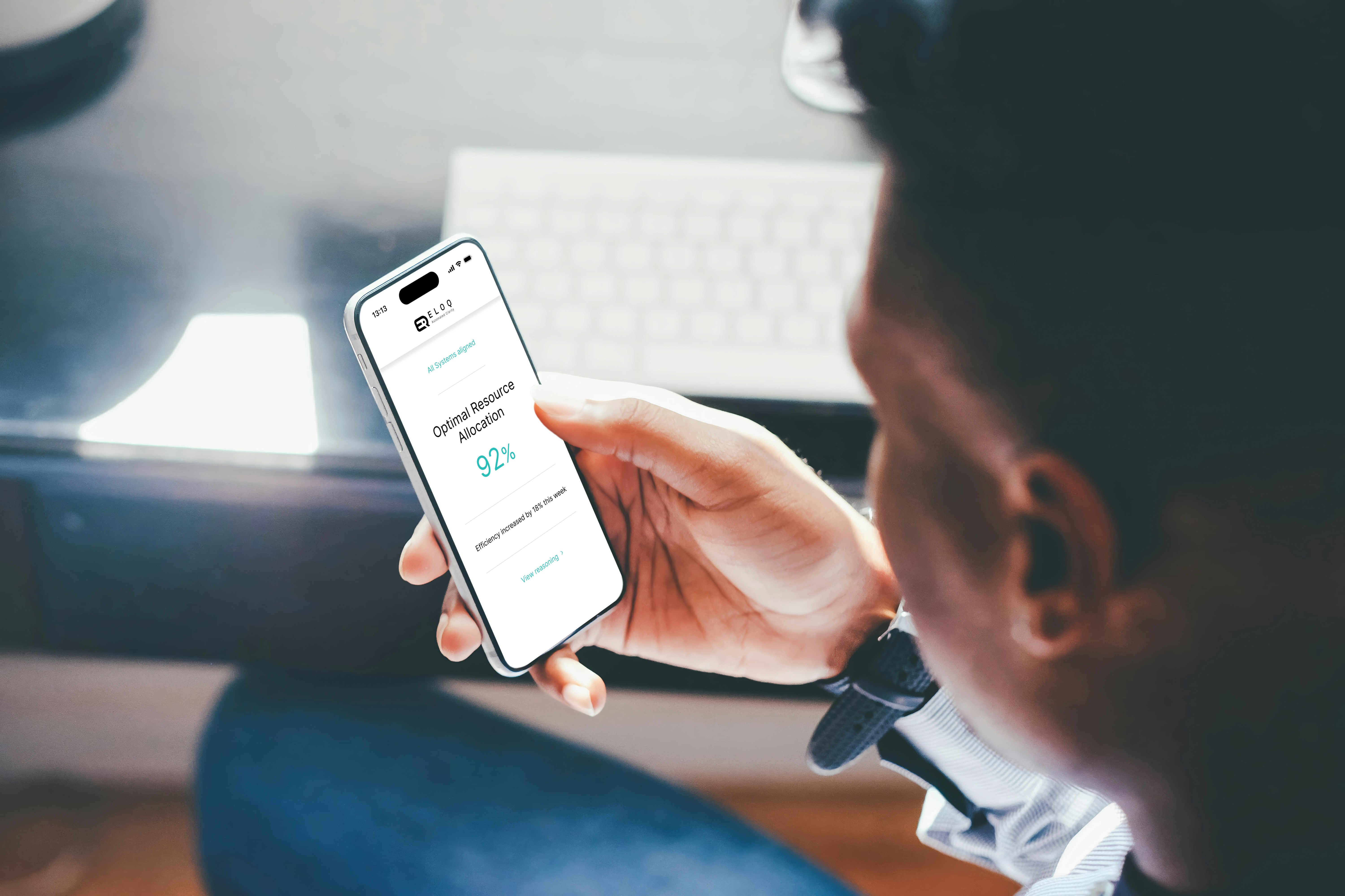 Eine Person hält ein Smartphone mit dem ELOQ Mobile Interface in der Hand. Auf dem Bildschirm wird eine Analyse zur optimalen Ressourcenzuweisung mit einem Effizienz-Wert von 92 Prozent angezeigt.