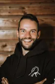 Lachende man met baard in een zwarte Broederschap-hoodie, de armen over elkaar