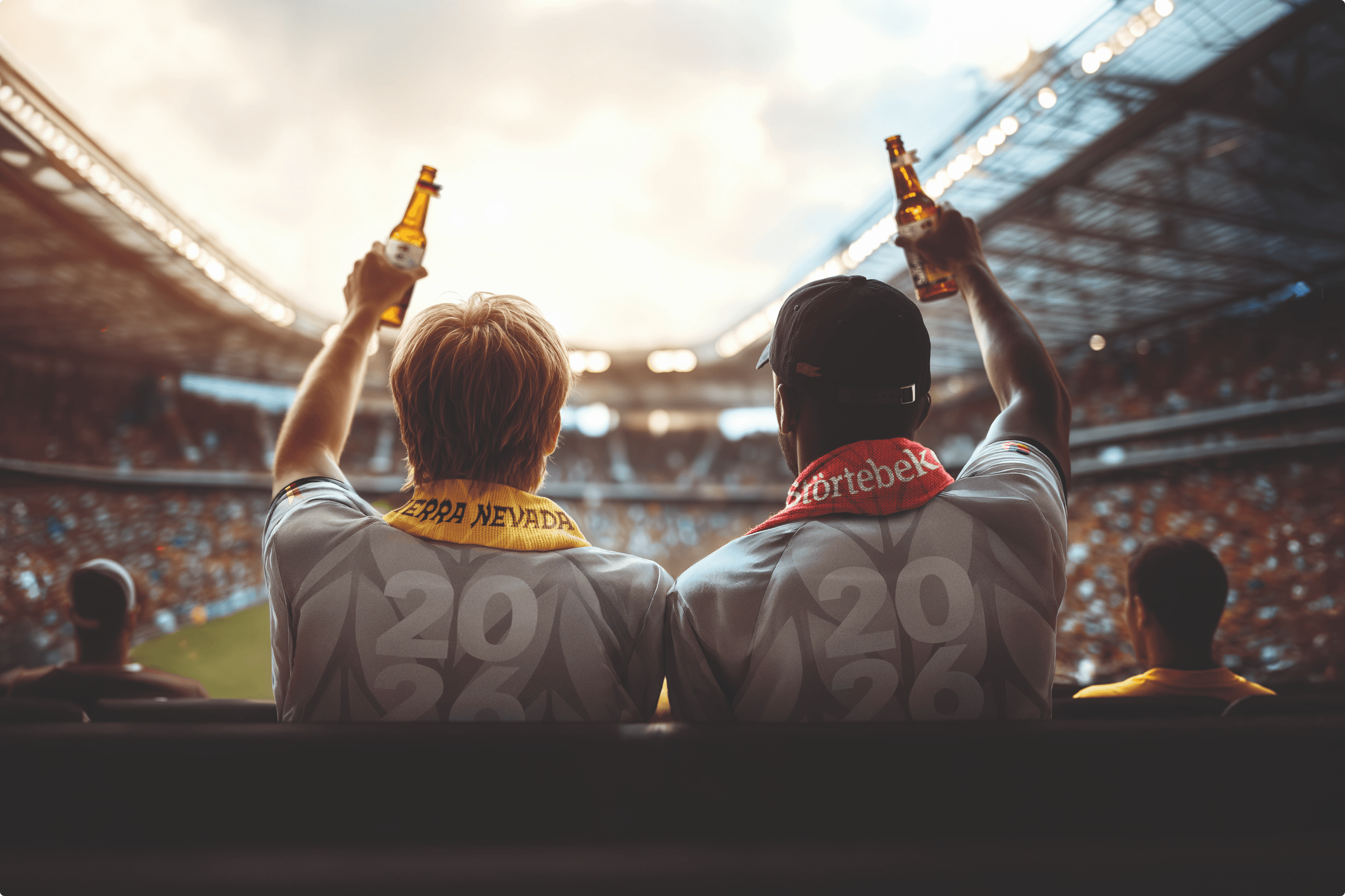 Two fans raise beer bottles at a stadium.