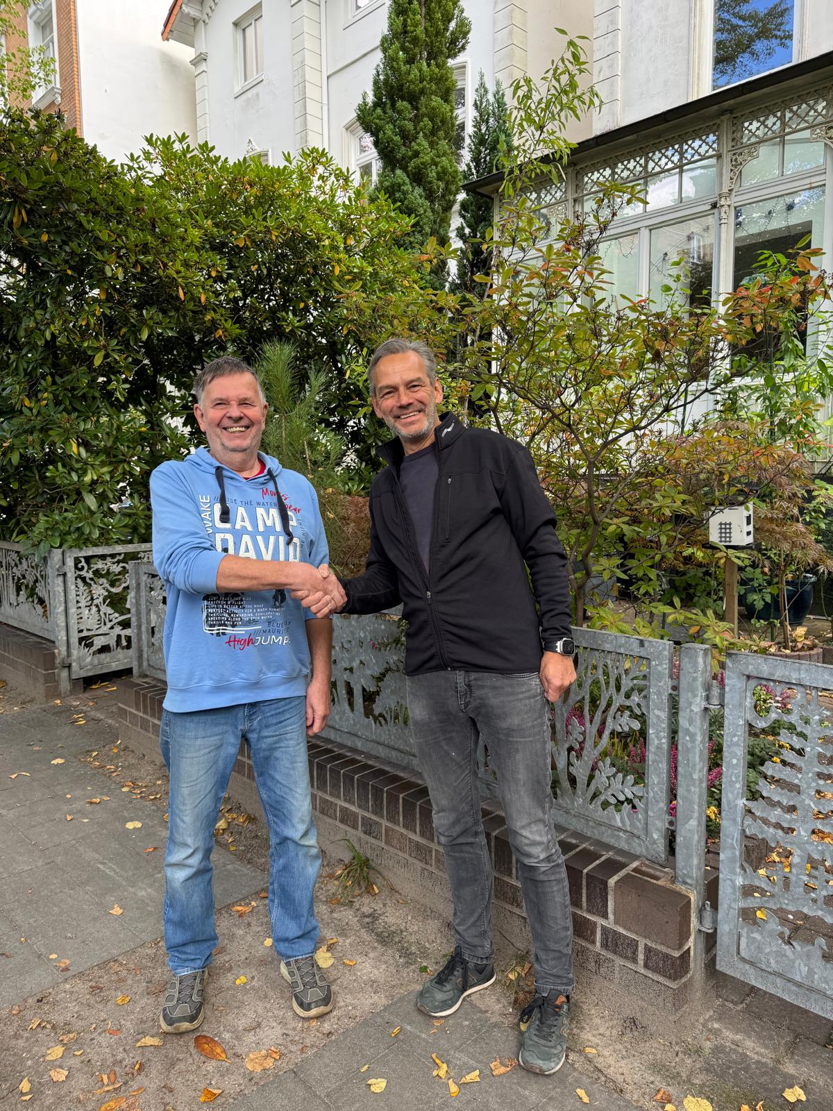 Smiling young woman with long hair standing against a dark green background, holding a finger to her chin.