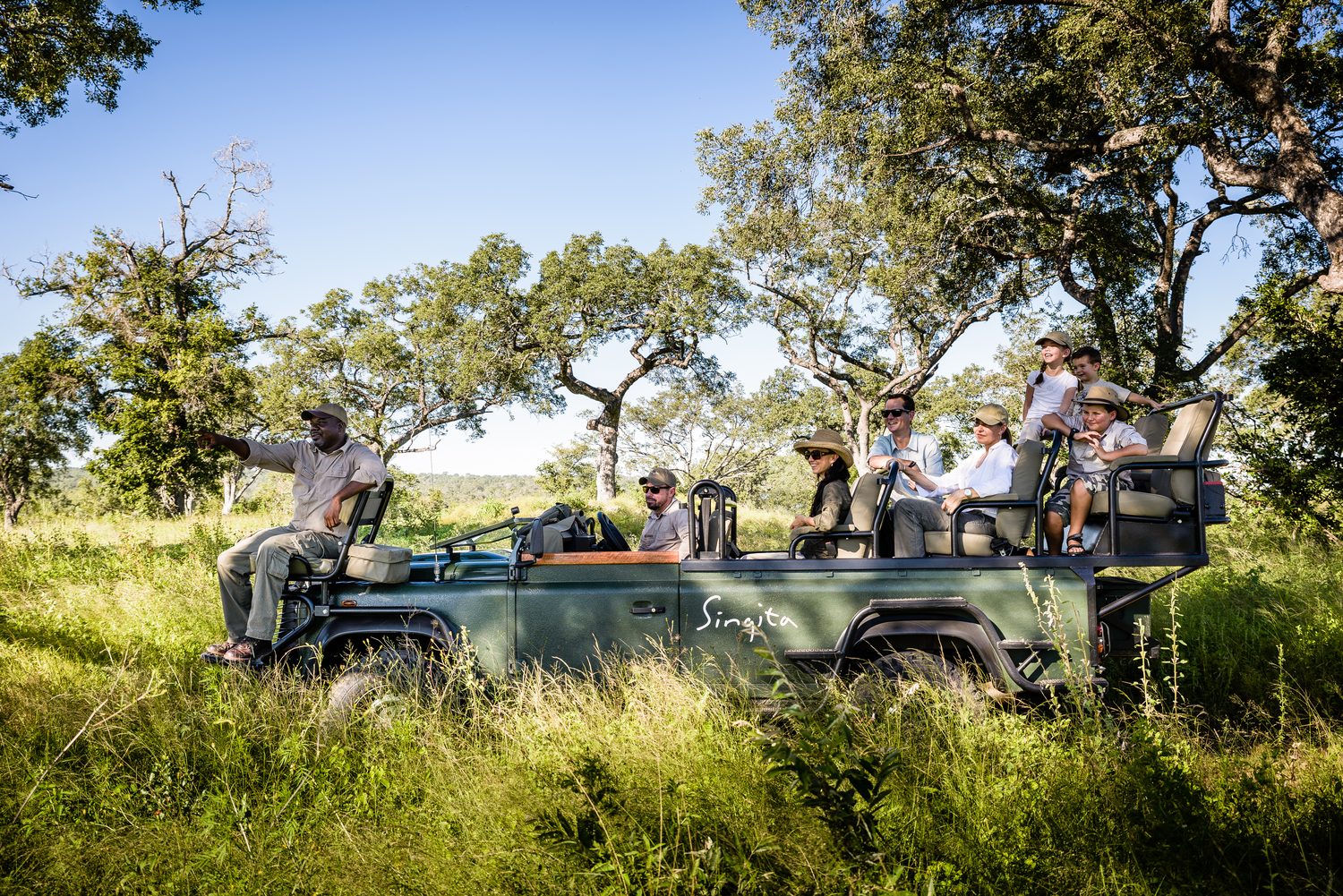 A guide pointing out game to a family aboard a Singita vehicle