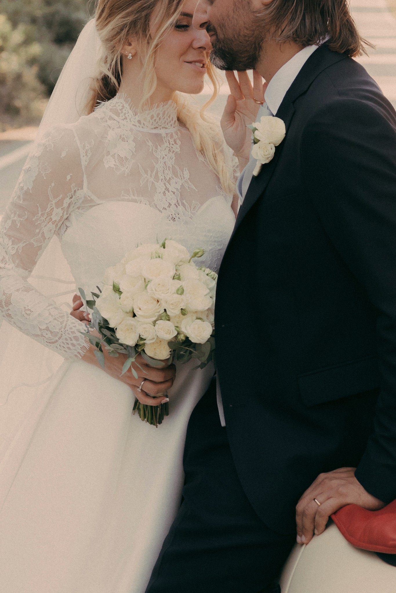 Sposi si baciano, lei in abito bianco con velo, lui in smoking, bouquet bianco in mano, luce dorata di Bolgheri