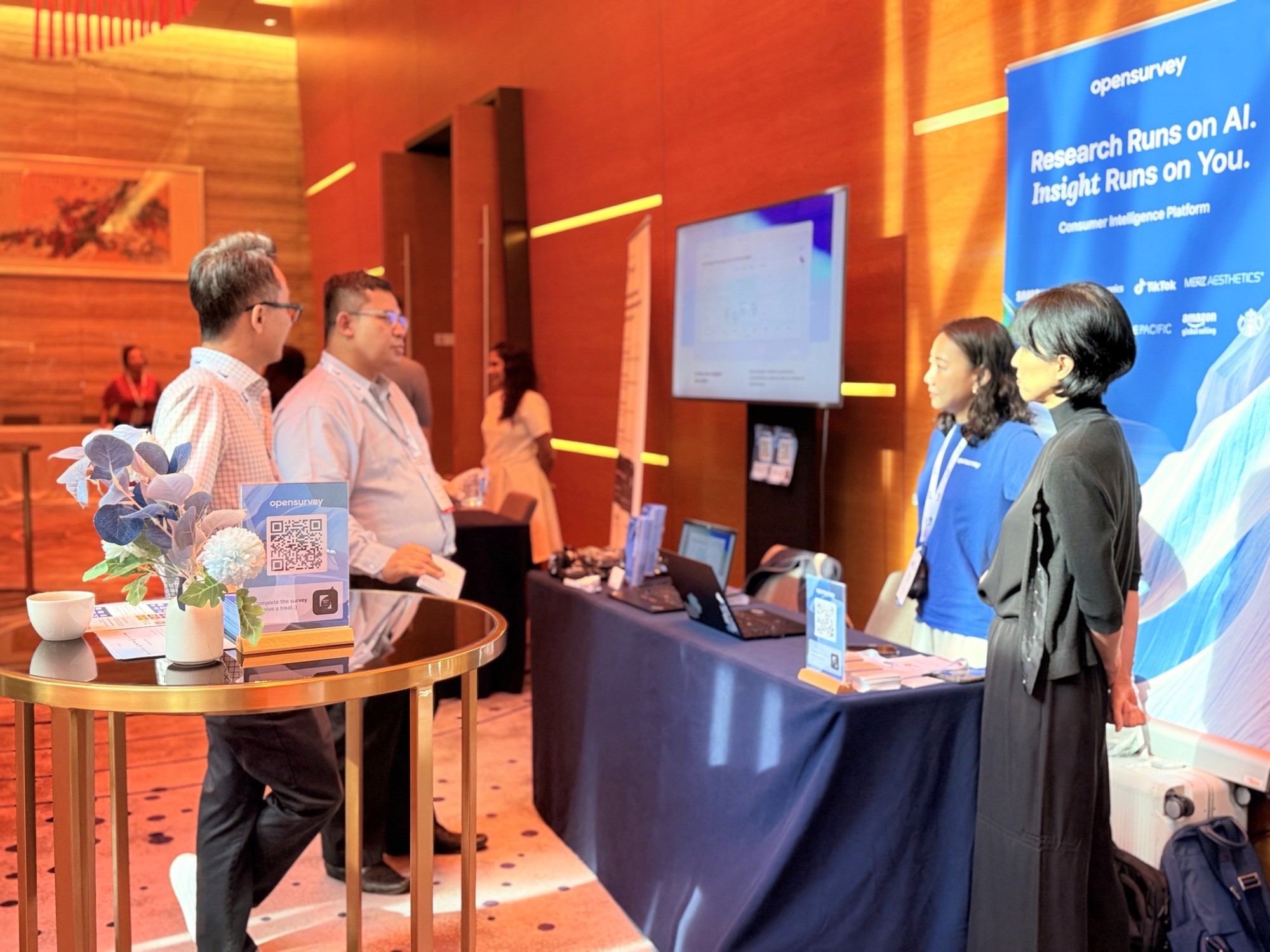 Two individuals engage at a booth, with displays and information in a brightly lit, modern setting.