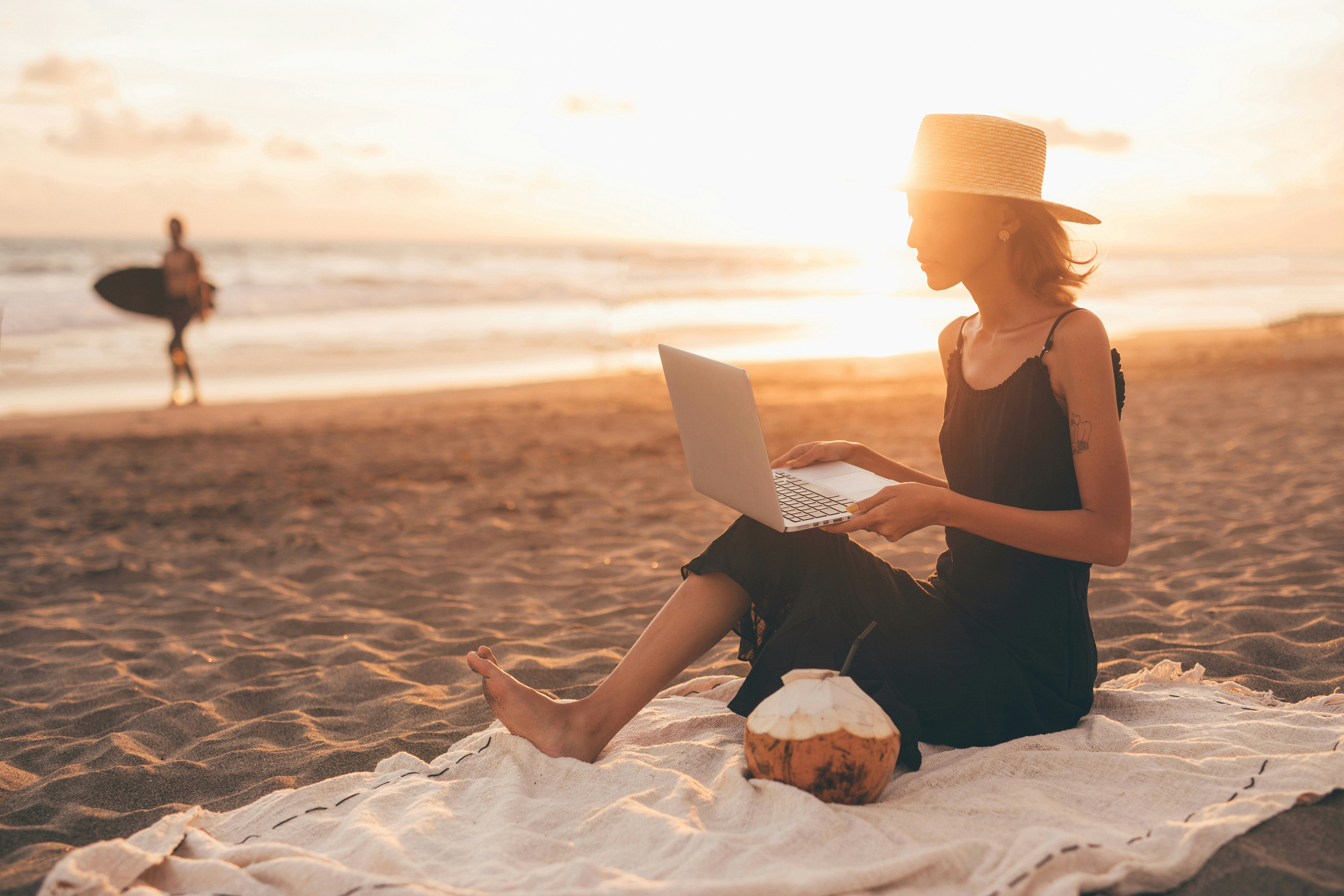 Eine Frau arbeitet mit einem Laptop am Strand bei warmem Abendlicht. Das Bild steht für digitale Freiheit, Fokus und automatisierte Klarheit jenseits klassischer Arbeitsräume.