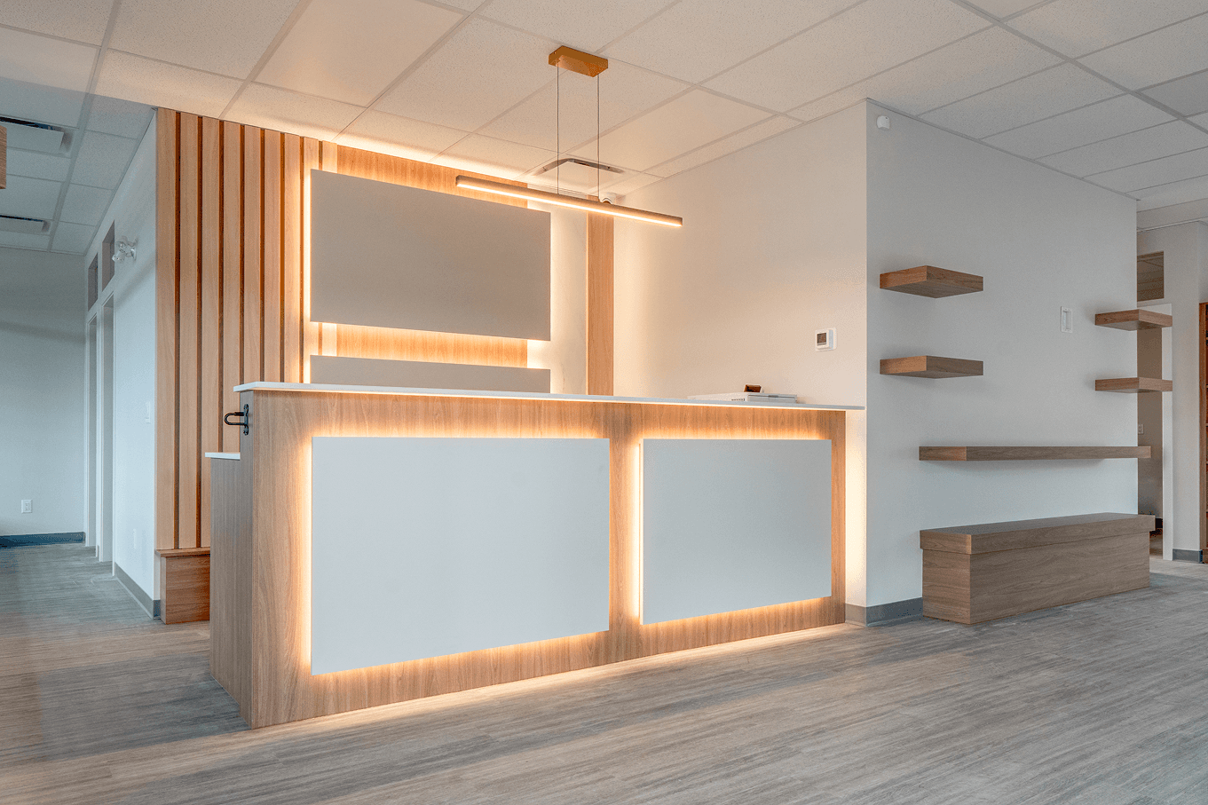 Modern reception desk with warm LED backlighting, wood panel accents, and minimalist wall shelving in a commercial space.