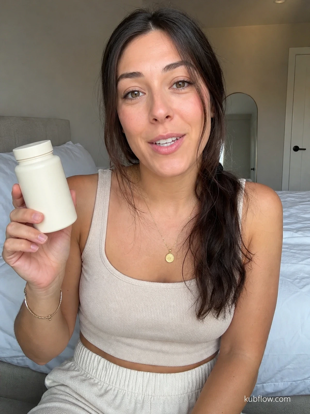 UGC-style photo: home cook creator, in a clean bedroom, holding a plain wellness product while talking to camera, phone-on-tripod angle.