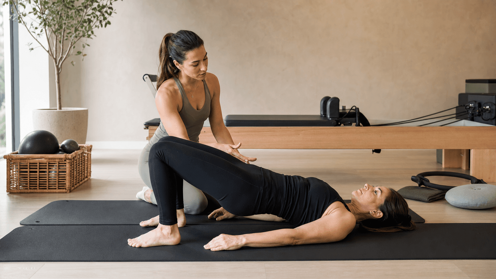 Instructrice de pilates guidant une élève sur tapis, accessoires dans studio.
