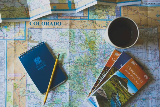 A flat lay of a map, a notebook, a pen, and a cup of coffee, suggesting travel planning or adventure.