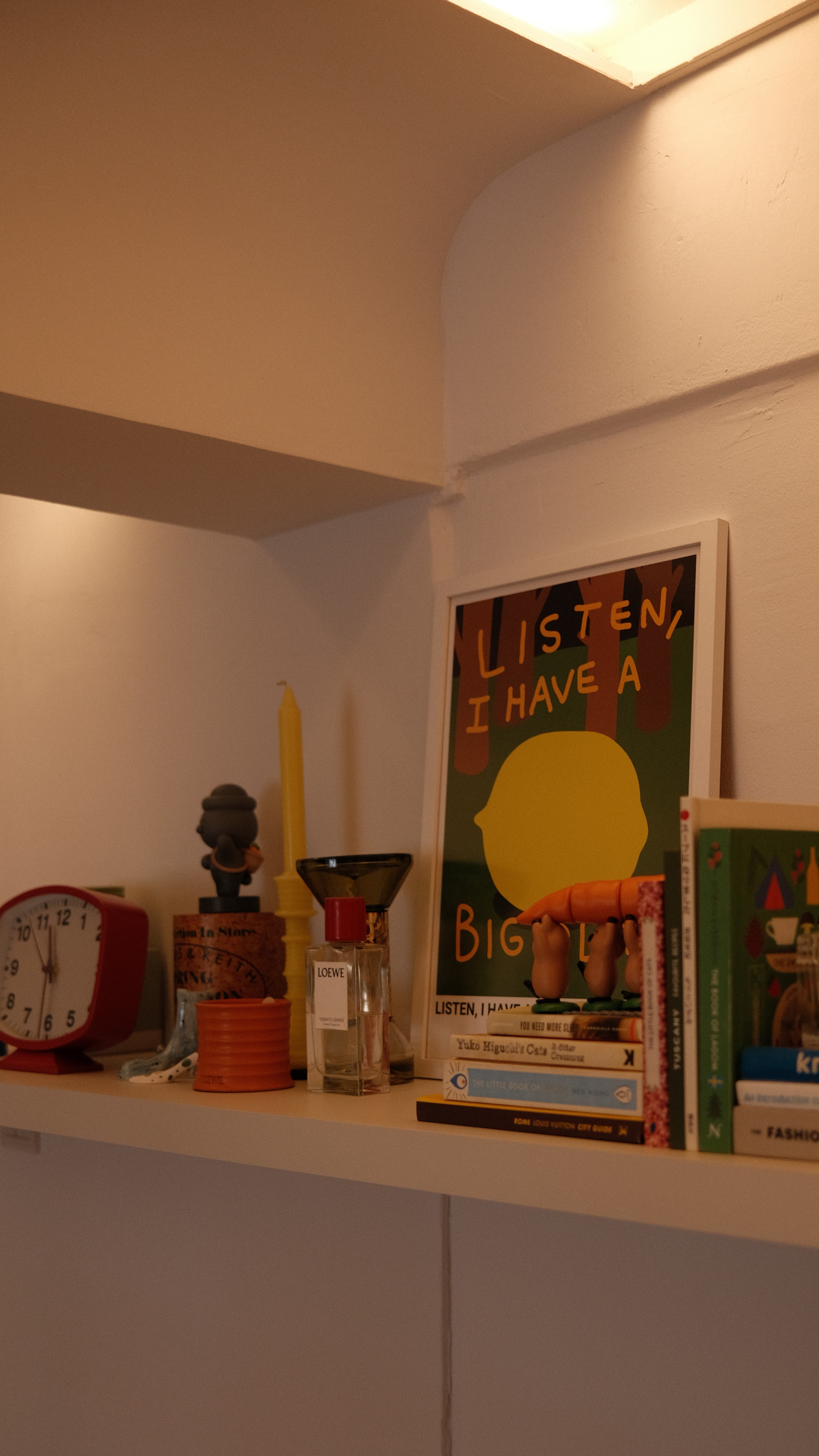Shelf styled with art print “Listen, I have a big lemon,” yellow candle, and eclectic books, showcasing modern playful decor in Holland C.