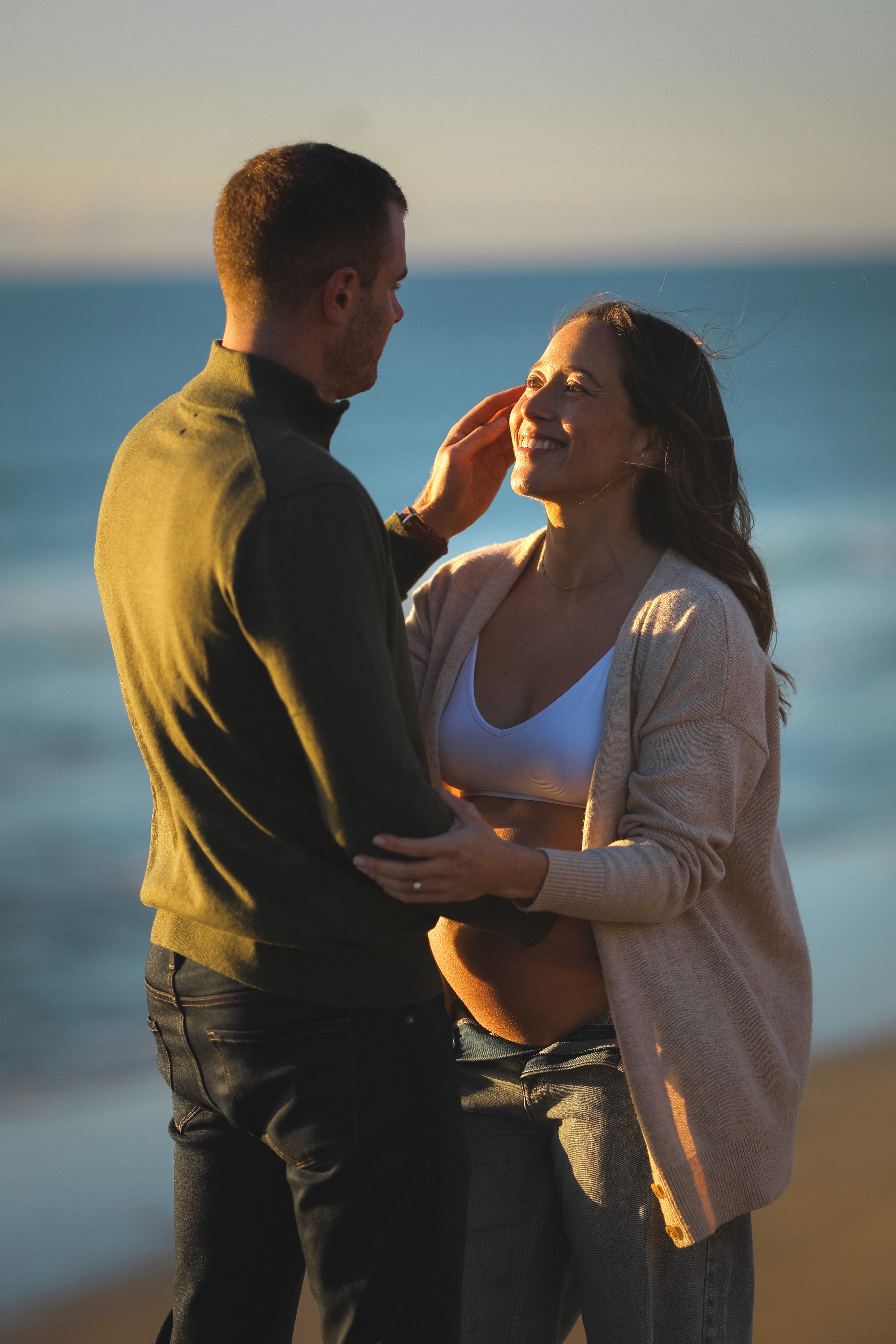 Couple hugging at the beach during a sunset maternity session in San Diego.