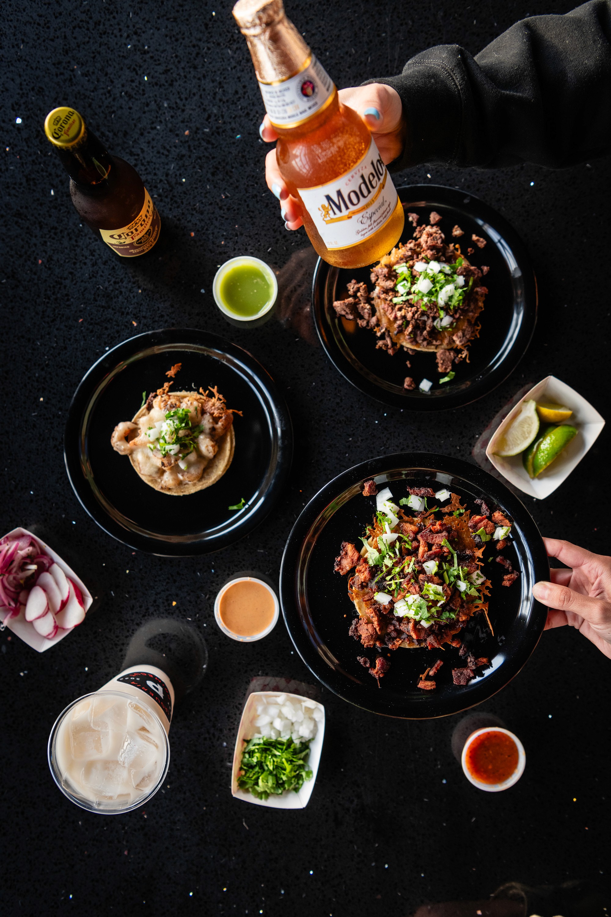 Primecut tacos, salsas, onions, and a beer on a black table
