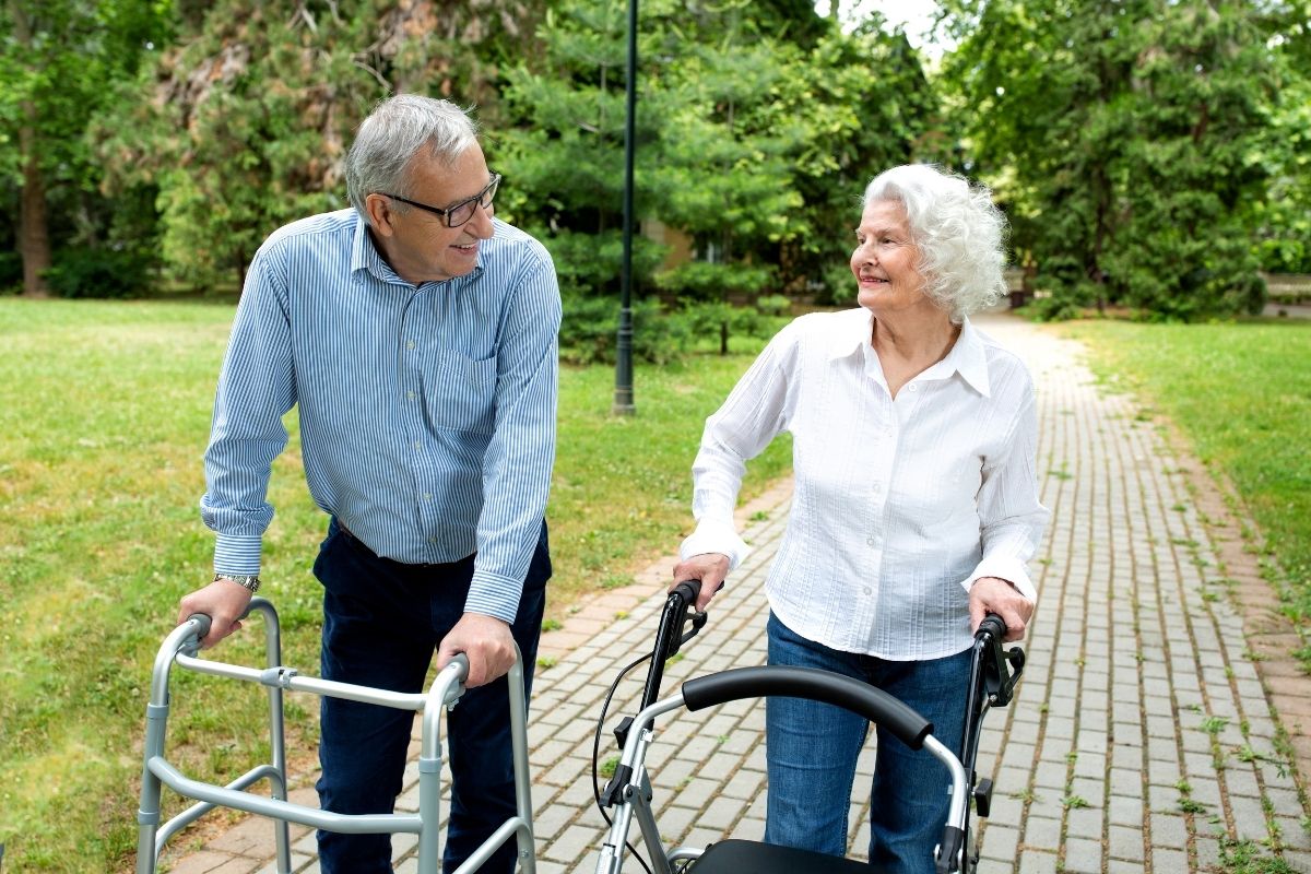 Elderly couple walking together using walkers.