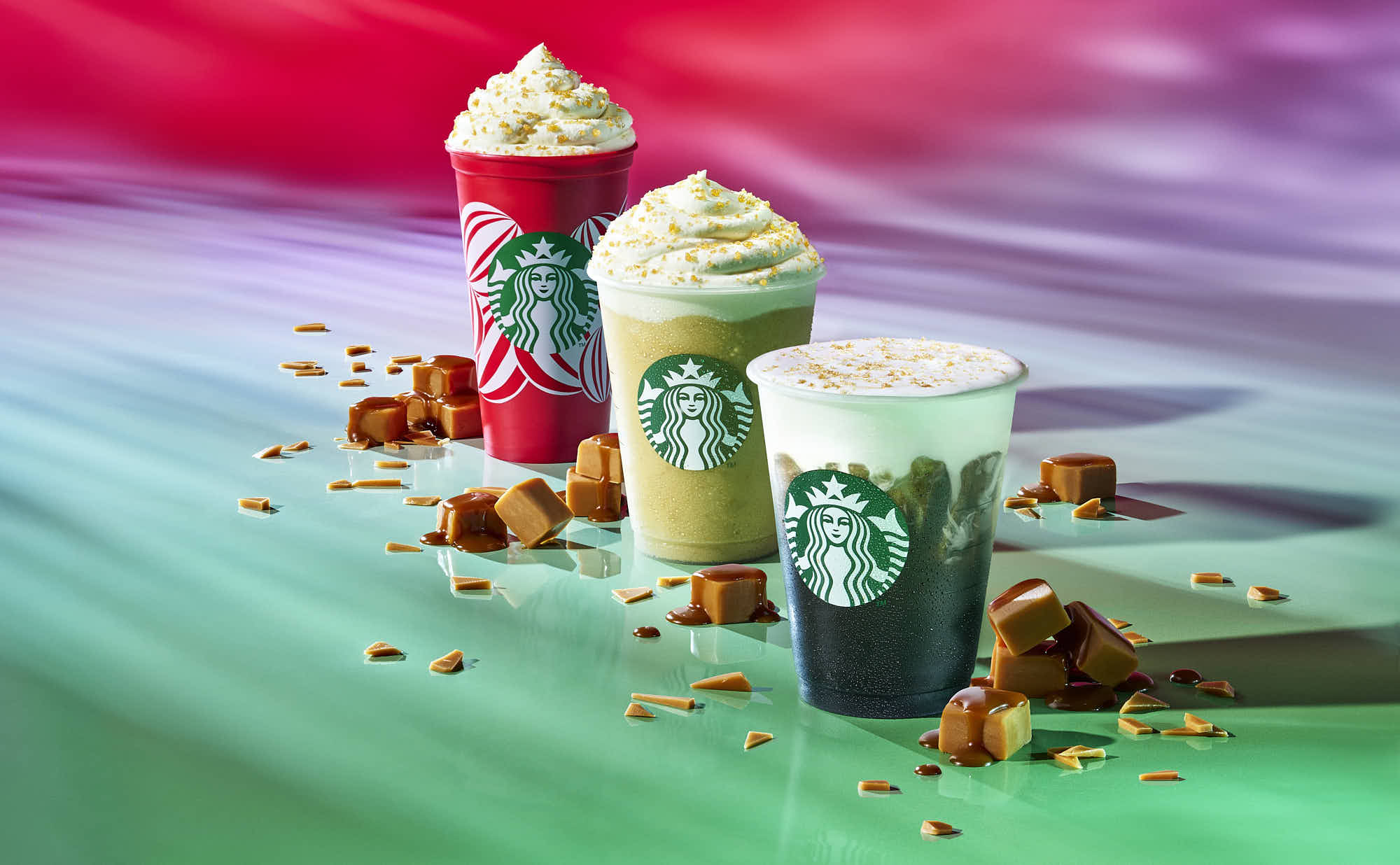 Three colorful iced coffees topped with whipped cream, placed on a vibrant, swirled background.