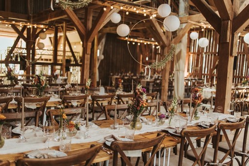 Festlich dekorierte Scheune mit rustikalen Mietmöbeln von fruchtbar mobil – runde Holztische und Crossback-Stühle für eine gemütliche Hochzeitsfeier.