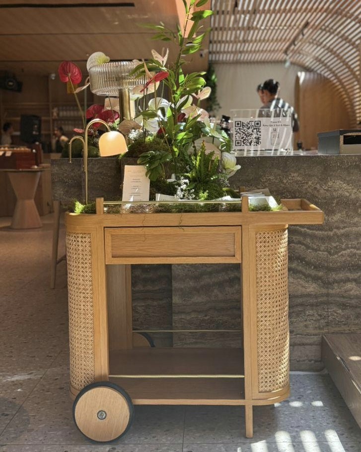 A wooden serving cart with intricate detailing, adorned with fresh flowers and greenery, positioned in a modern dining space.
