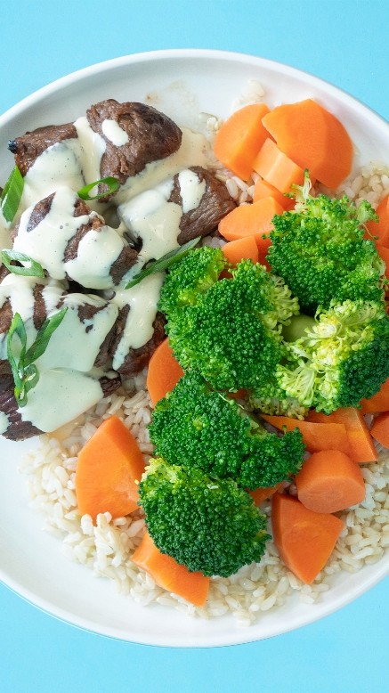 Plate of hibachi steak bites on a bed of rice, with roasted carrots and broccoli on a blue background 