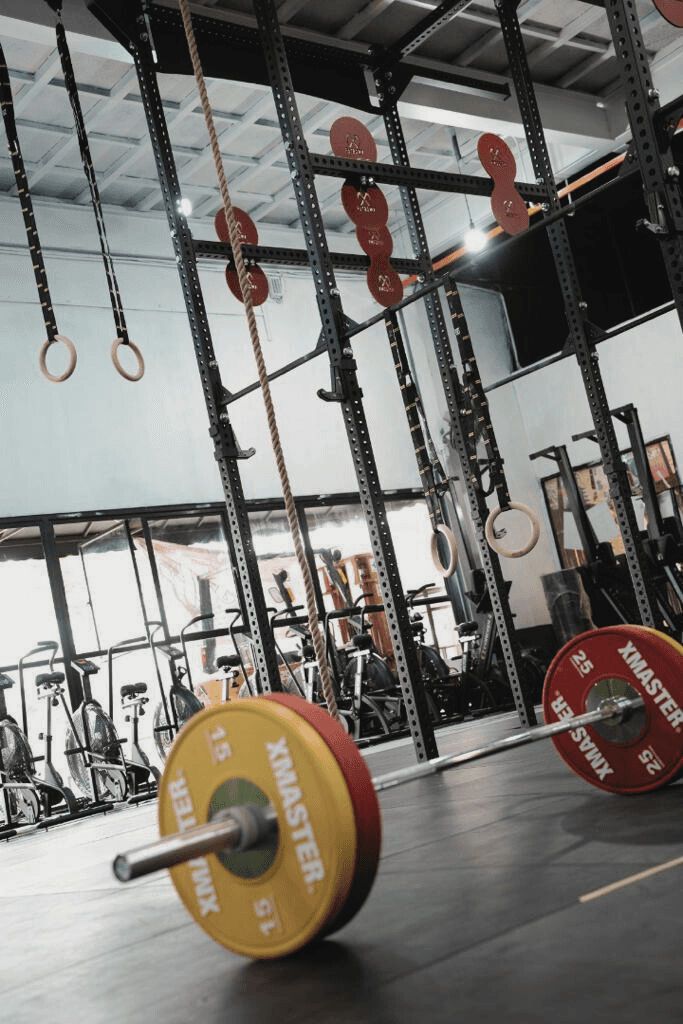 A man with defined abs holding onto a vertical pole in a gym, looking to the side.