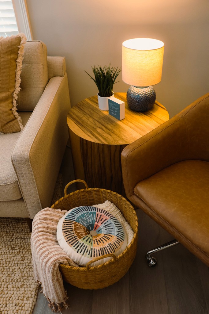 Side table with lamp, small plant, woven basket, and folded throw blanket.