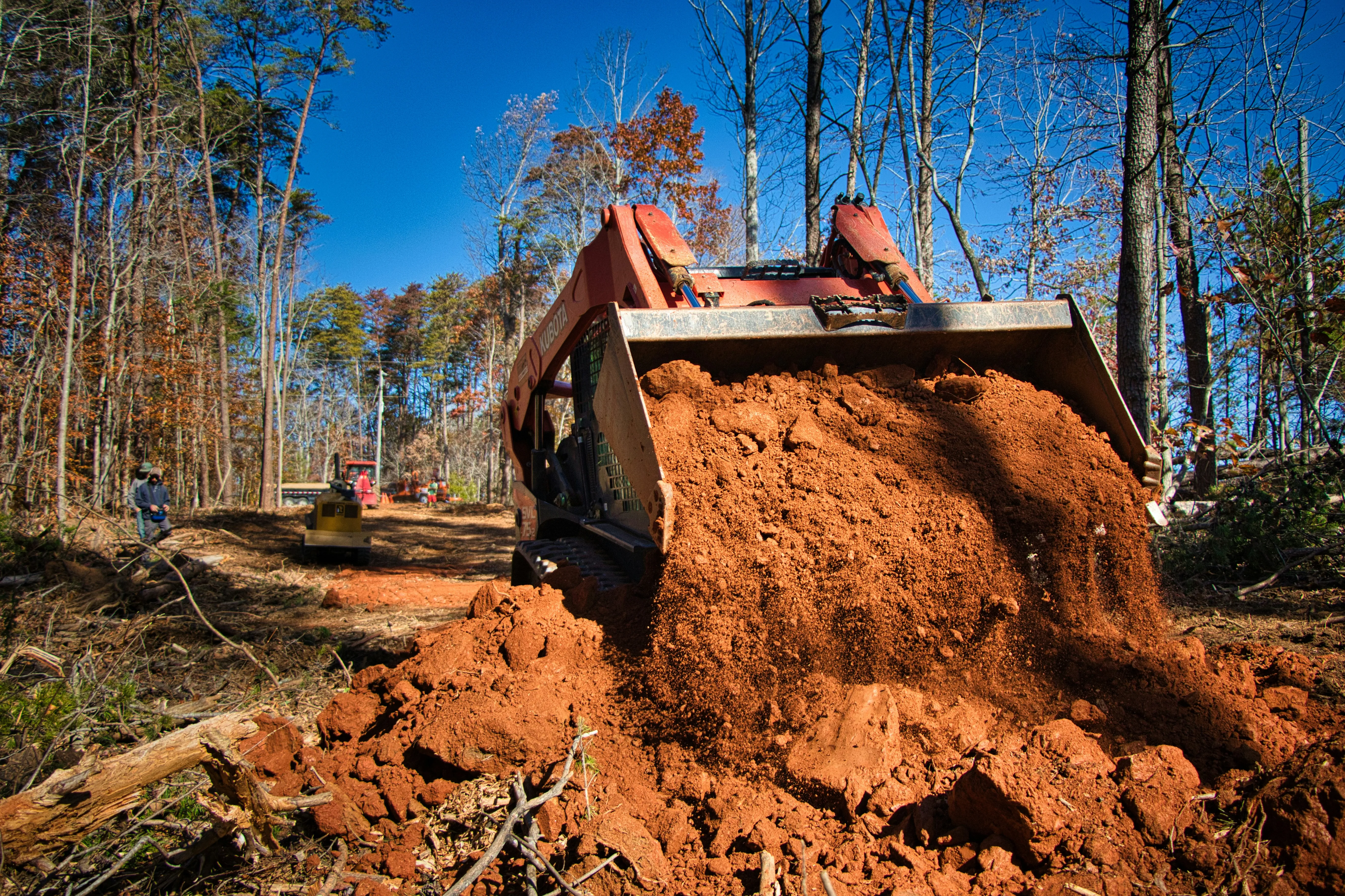 Skid steer loader moving dirt in a wooded area