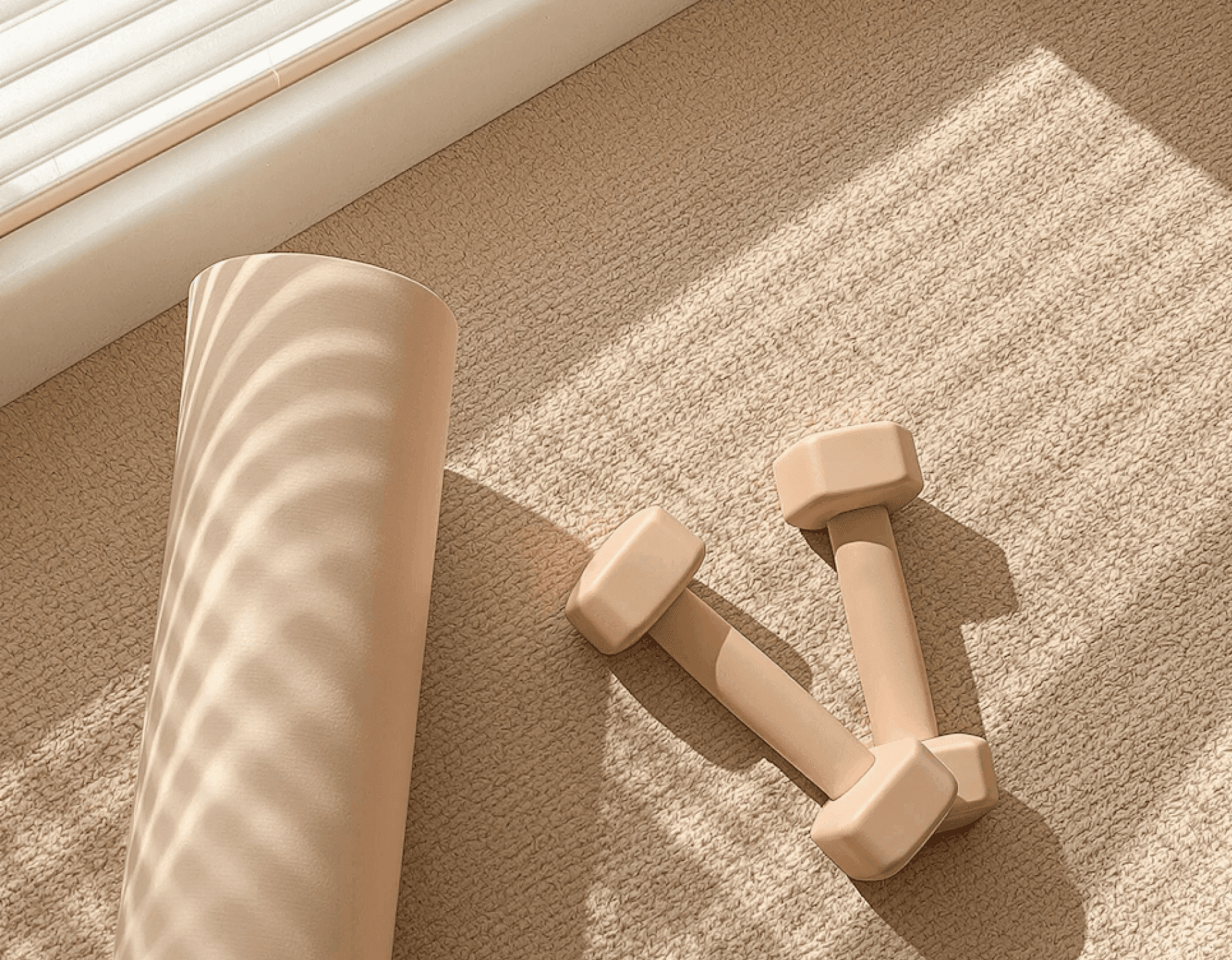 Soft sunlight over a yoga mat and dumbbells on a beige textured floor.