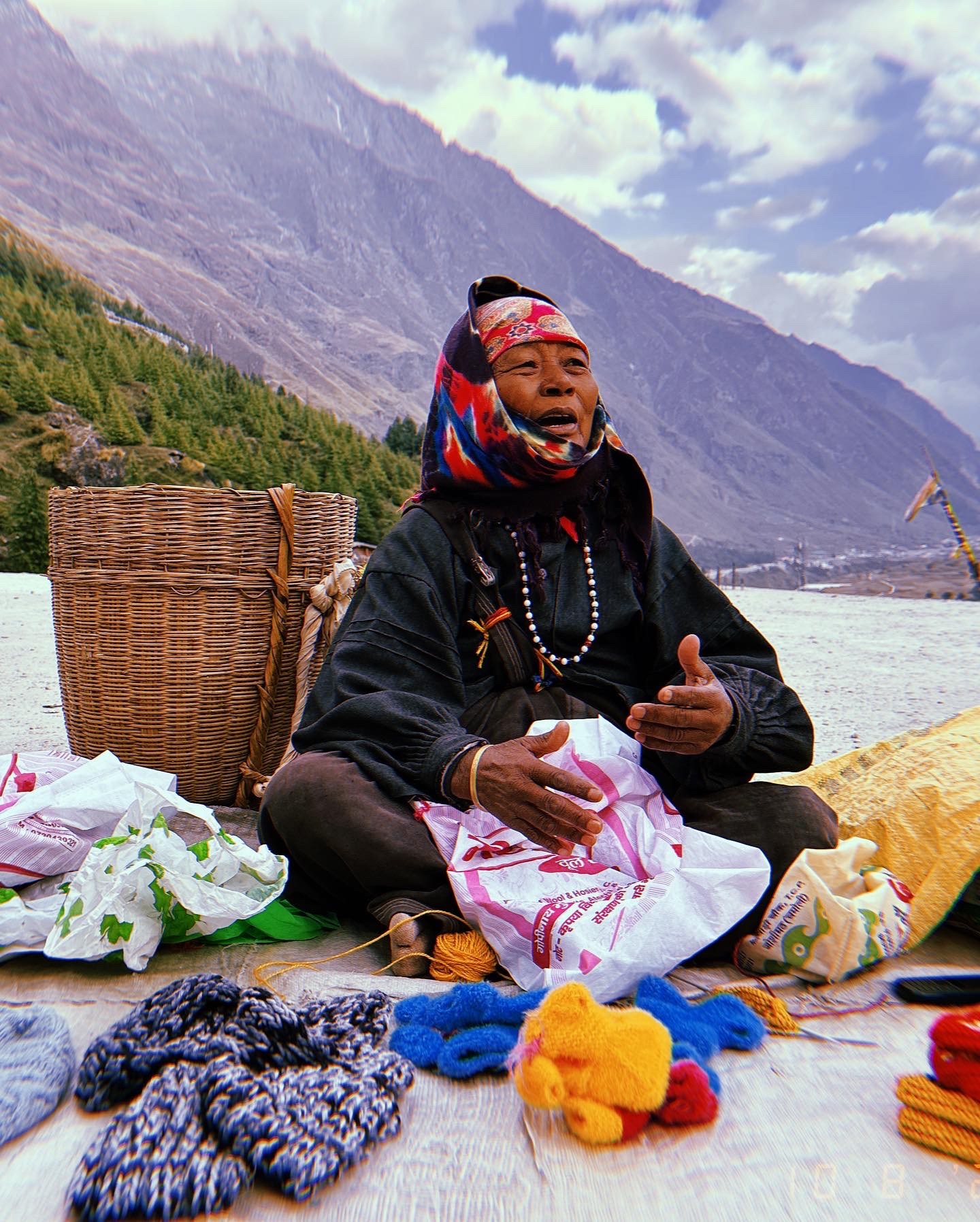 Seated bead seller beside the river with mountains behind