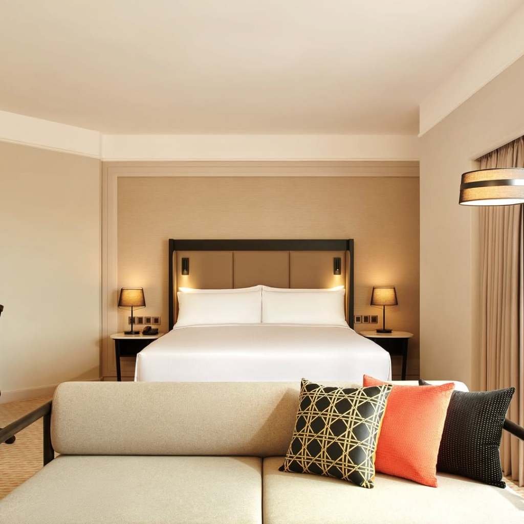 A modern hotel room at Hilton Kuching featuring a king-sized bed, stylish decor, and a comfortable seating area with decorative pillows.