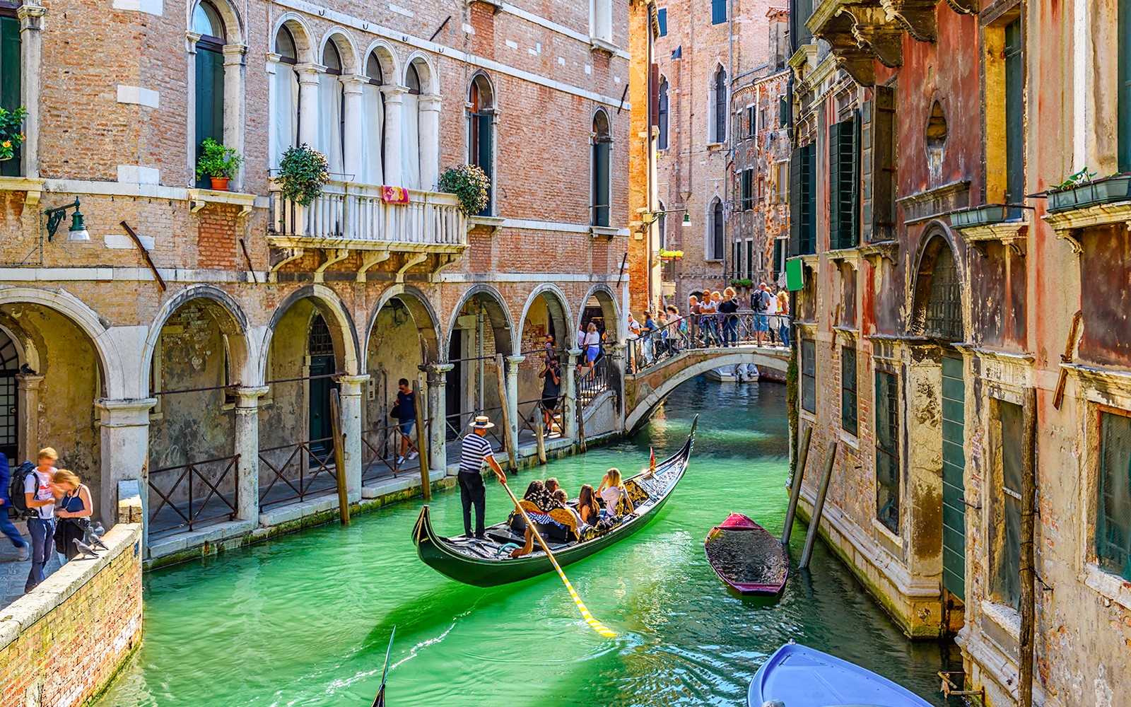 שיט בגונדולה מתחת לגשר אבן על תעלה צרה בוונציה, איטליה.