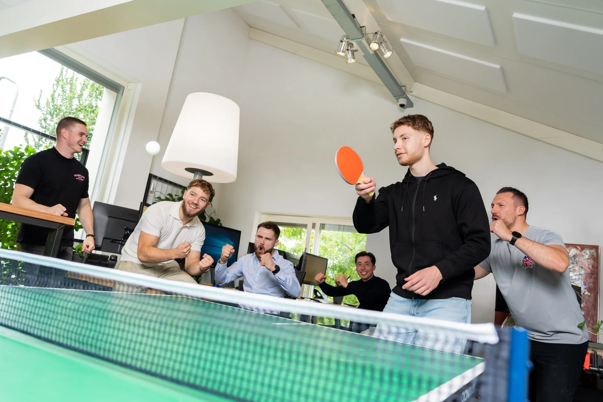 Iemand die aan het tafeltennissen is en mensen die hem aanmoedigen