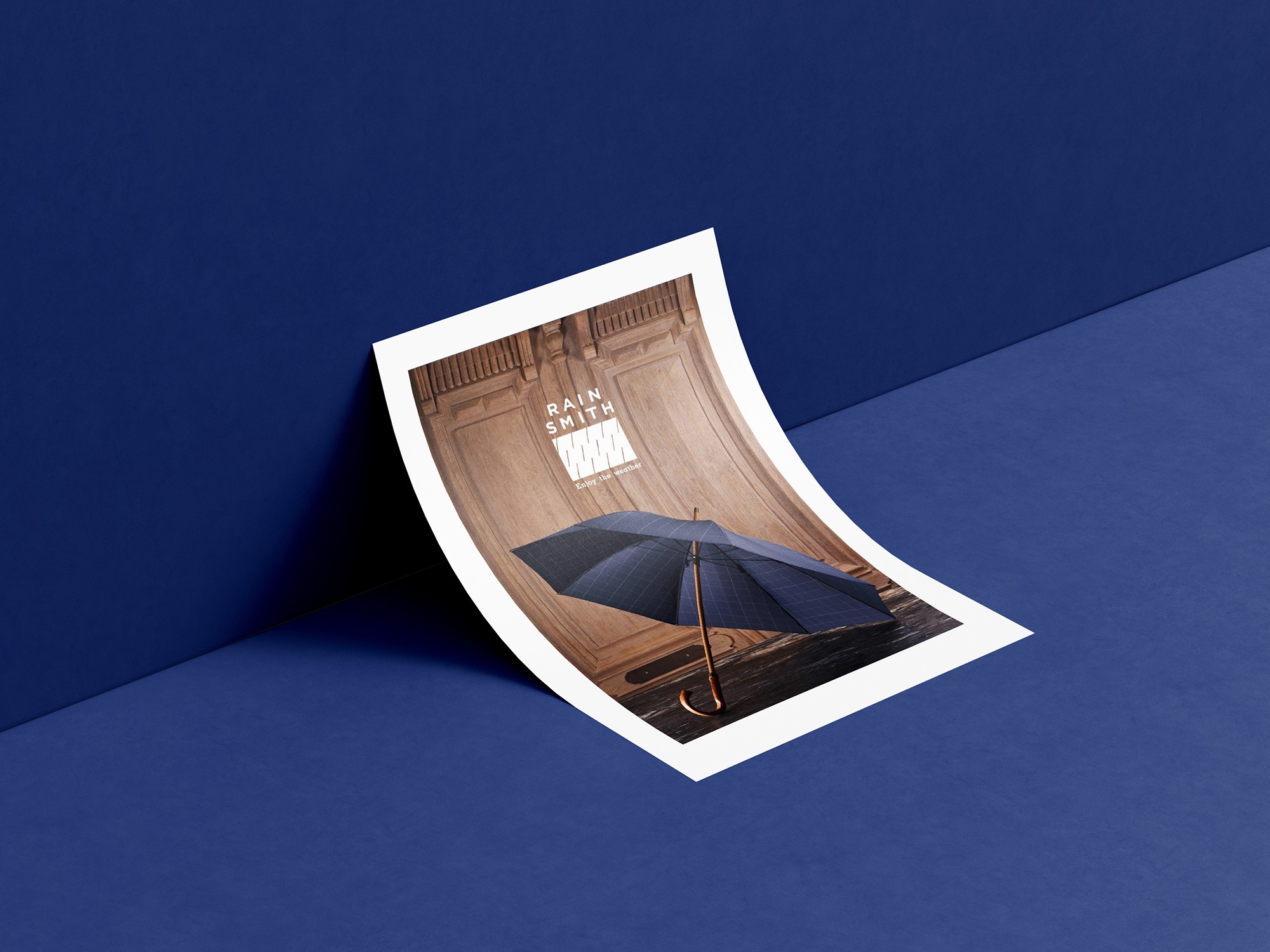 這張圖像展示了 RainSmith 的文宣圖,圖上有一把藍色雨傘,背景是木門,海報上方印有 RainSmith 的品牌識別和 "Enjoy the weather" 字樣。