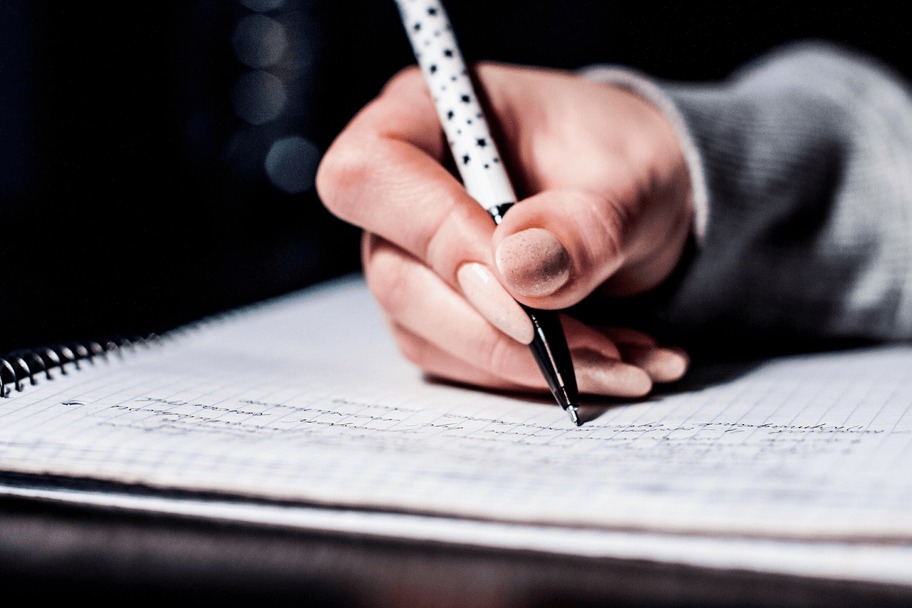 High school student writing optional college application essays at a desk with university brochures