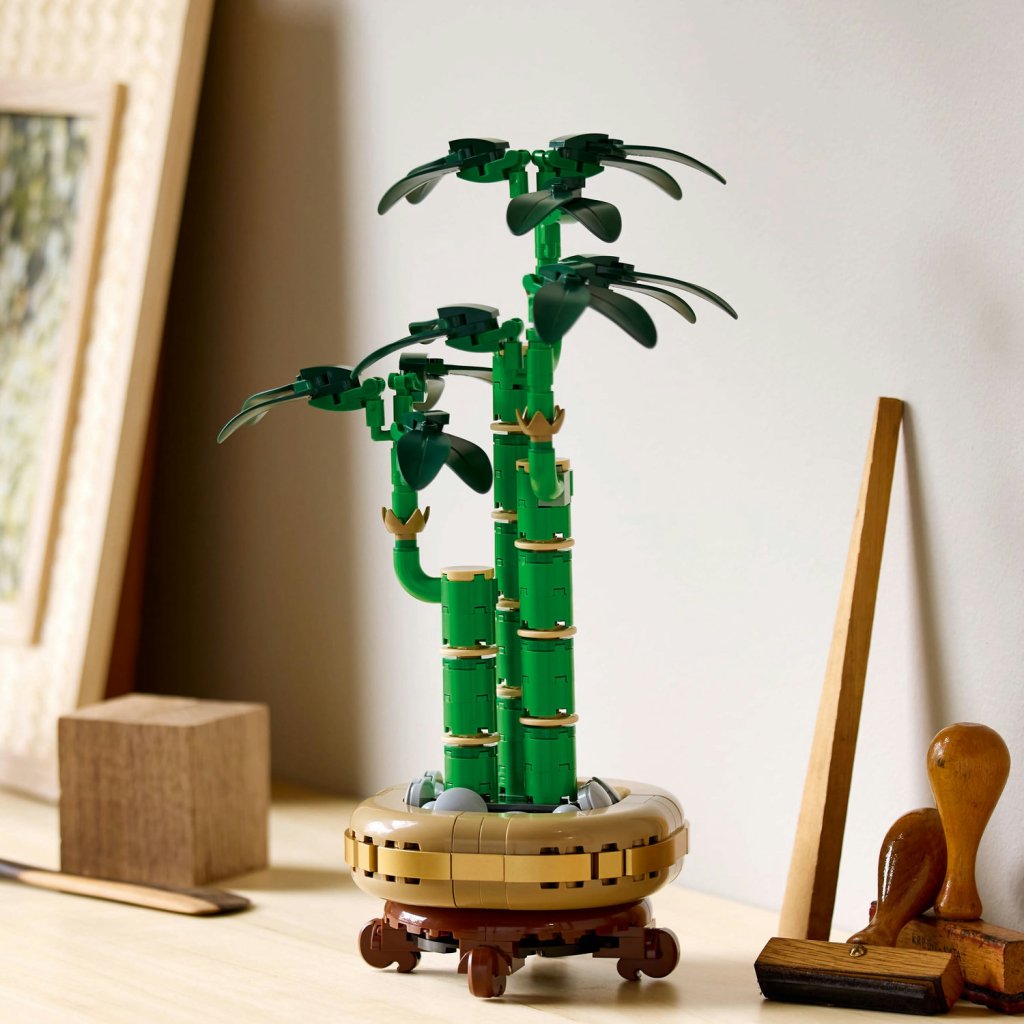 A LEGO model of a bamboo plant with green leaves, set on a circular base, displayed on a wooden surface next to other decorative items.
