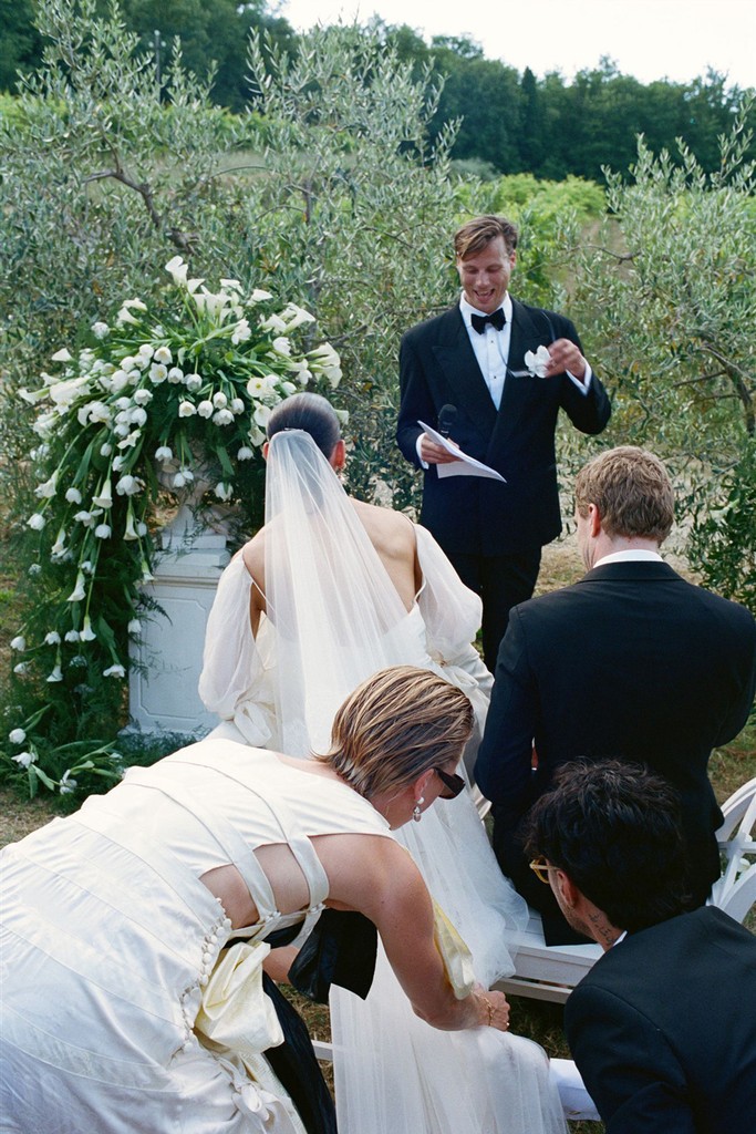 Wedding officiant reading welcome as the couple takes their seats and bridal party helps arranging veil 