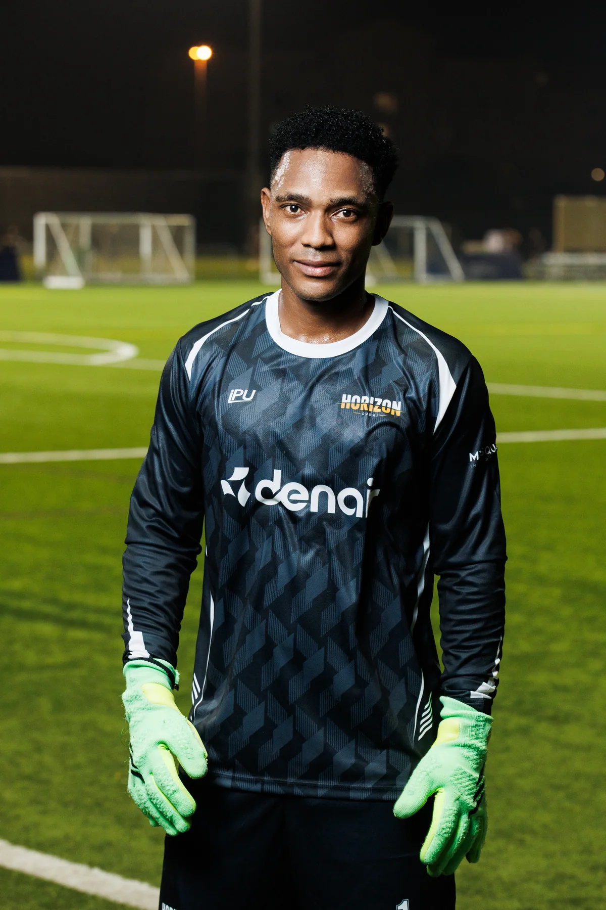 Horizon FC goalkeeper on a floodlit pitch, wearing a dark shirt with DENAIR branding and bright green gloves.