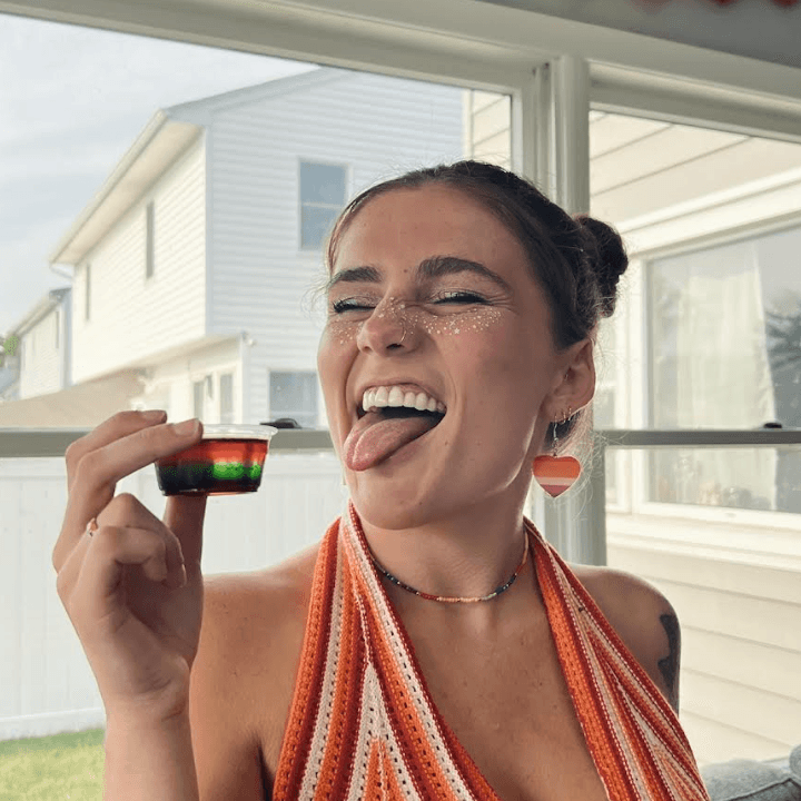 A woman in a striped top smiles and holds a colorful candy, with a playful expression, indoors.