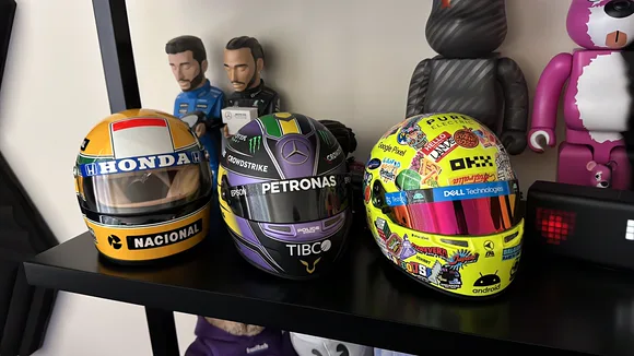 A shelf of collectibles including three Formula 1 mini helmets, driver figures and Be@rbrick toys.
