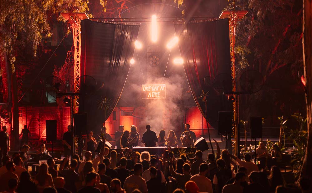 DJ booth view at ODAAT party with glowing orange lights and energetic crowd dancing late into the night.