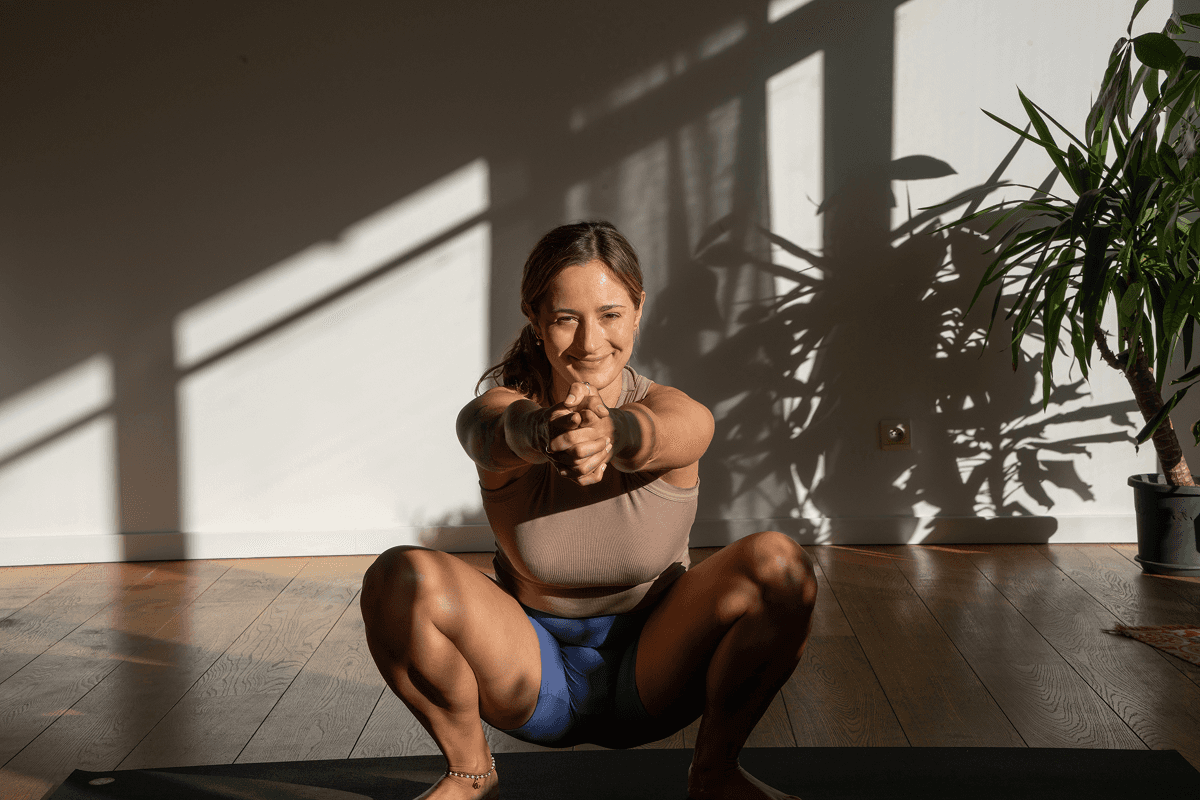 A person is practicing a squat exercise in a sunlit room, with wooden floors and a potted plant nearby, promoting mindful habits and a healthy, balanced lifestyle.